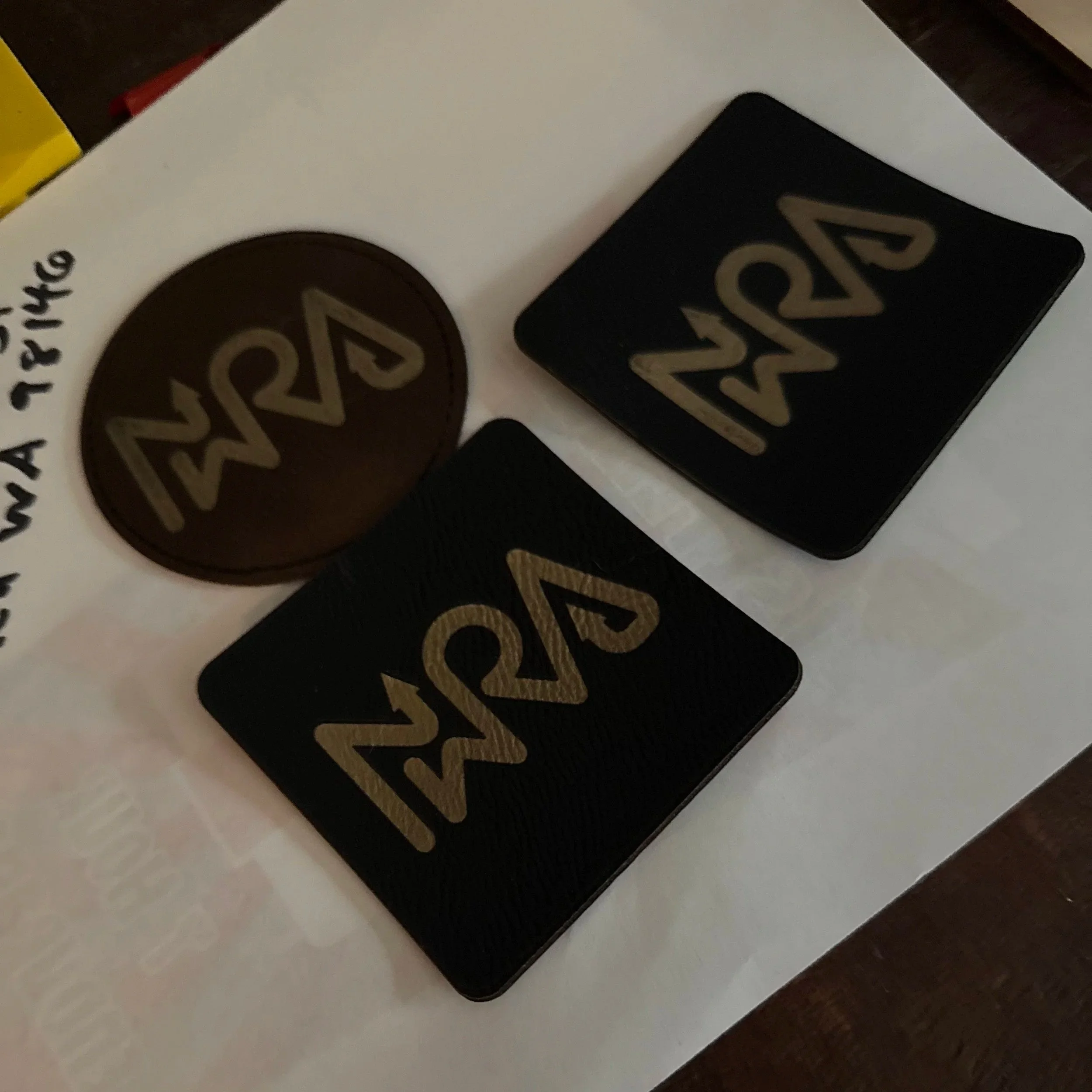 Two black tiles and a round sticker with gold-colored '24' logo placed on white paper on a wooden surface.