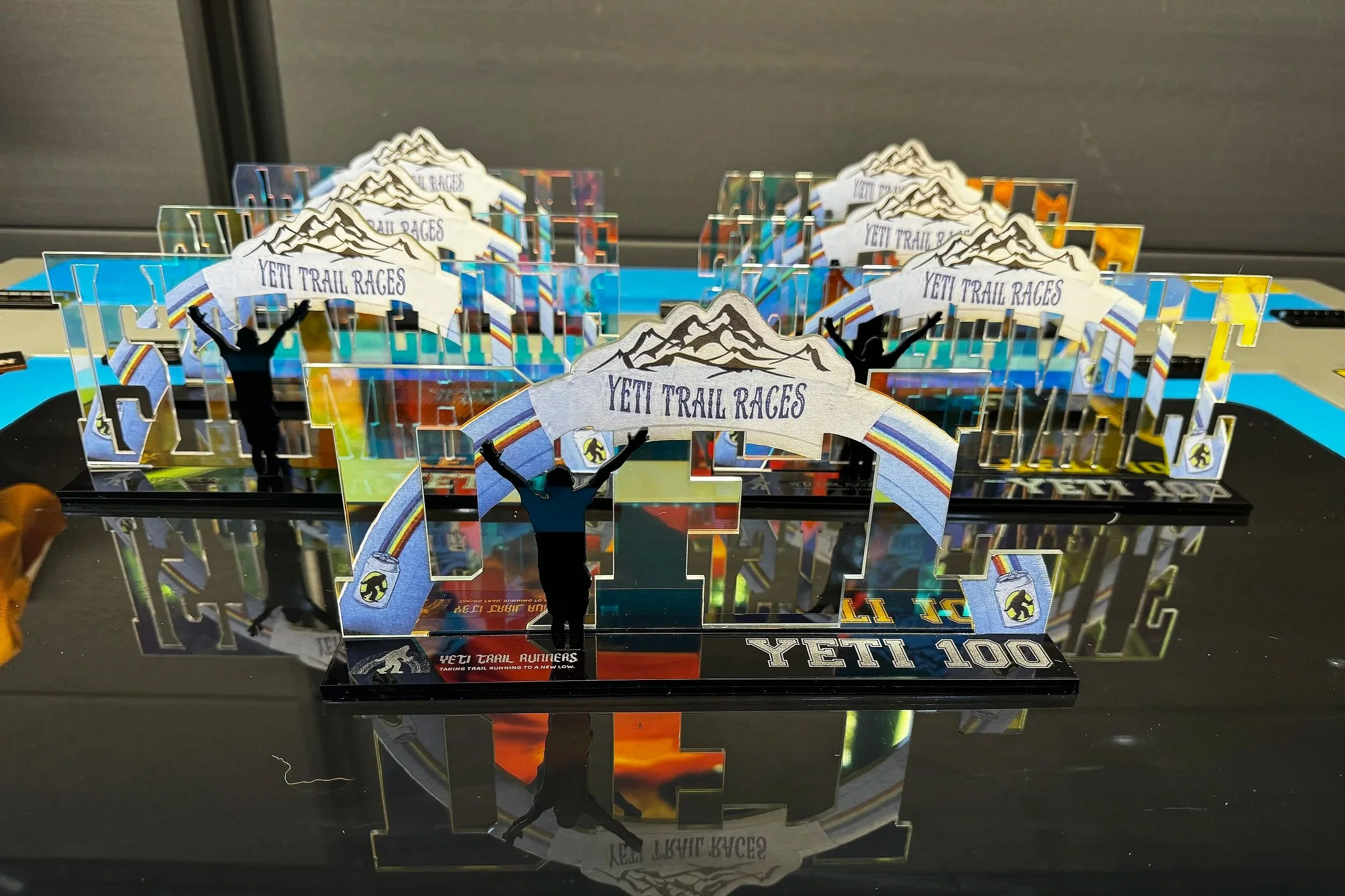 Decorative trophies for Yeti Trail Races featuring a mountain and runner silhouette with a banner, set on a reflective surface
