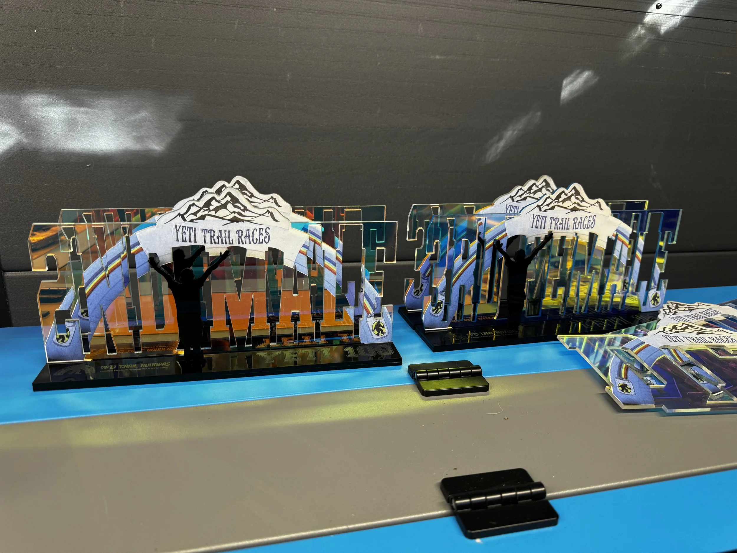 Various colorful trophies for Yeti Trail Races, featuring mountain designs and silhouettes of runners, displayed on a table.