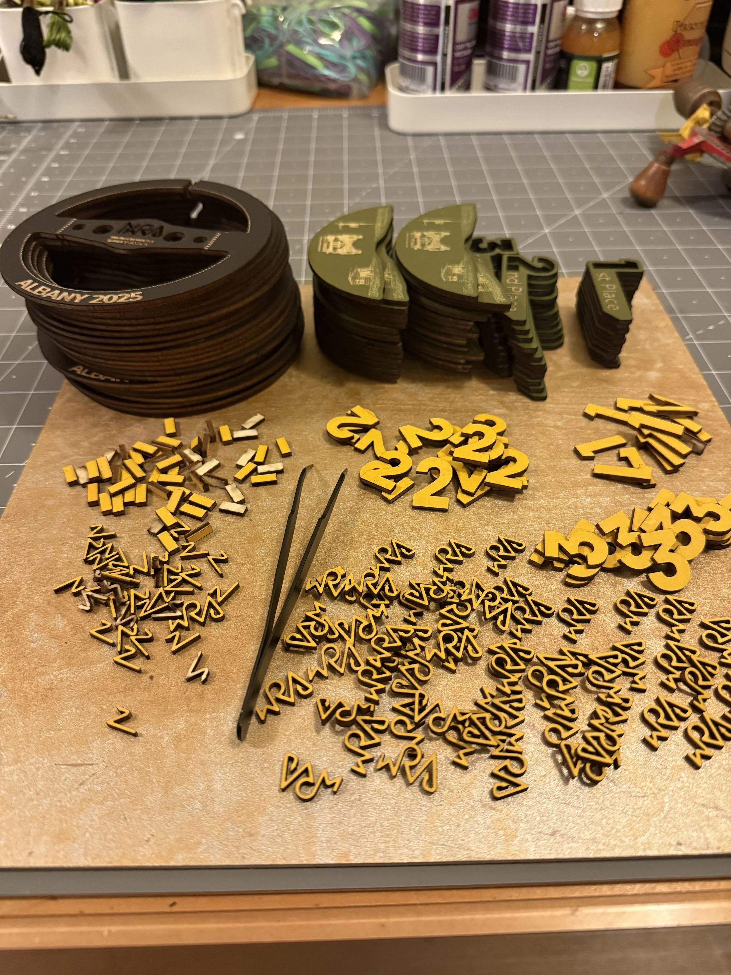 Numerical race bibs, small plastic racing icons, and tweezers arranged on a work surface for event preparation.
