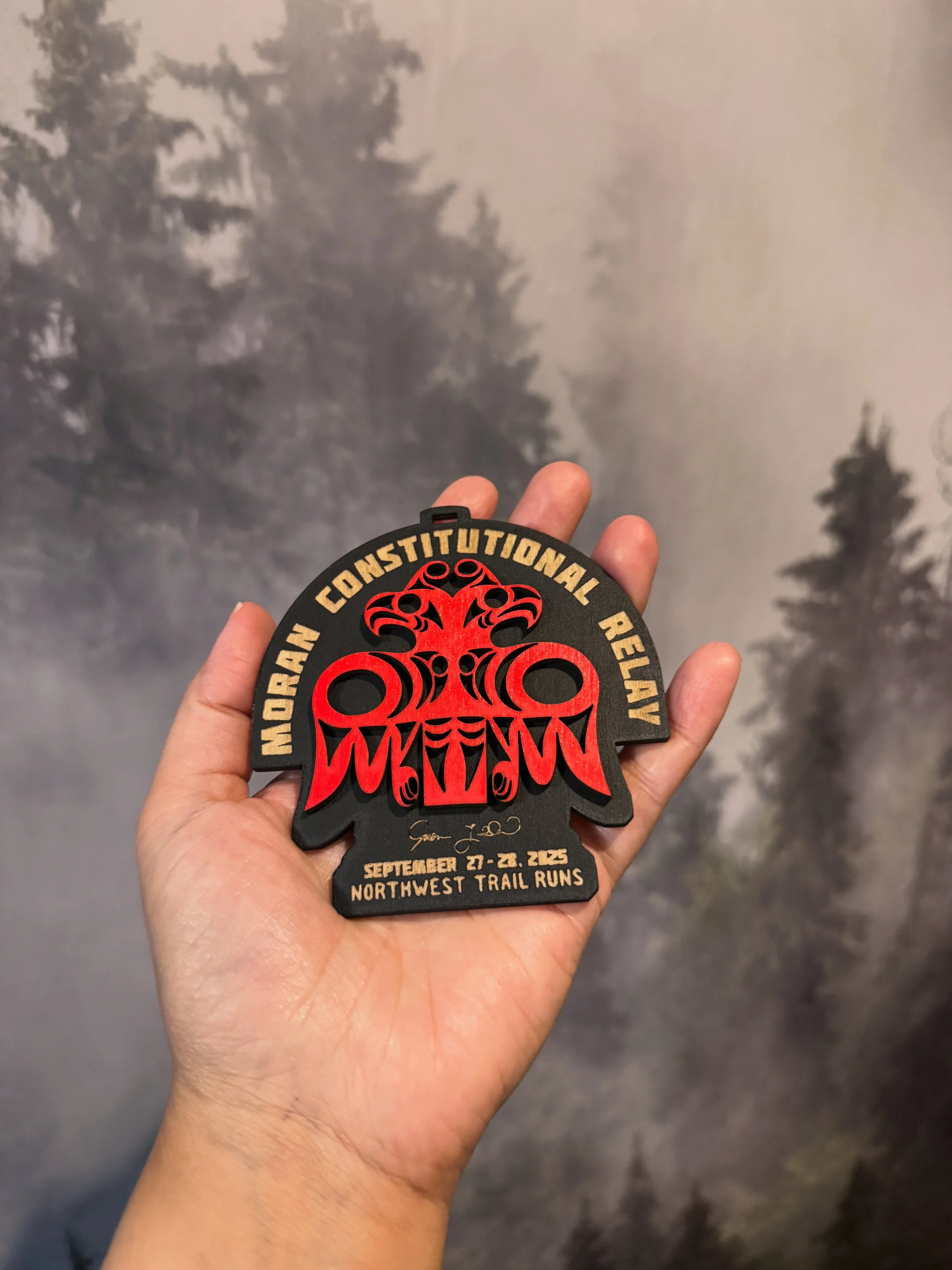 A hand holding a patch with the text 'North Constitutional Rally'. The patch features a red and black design of a stylized eagle, and details of the event held from September 21-24, 2023, at Northwest Trail Runs.