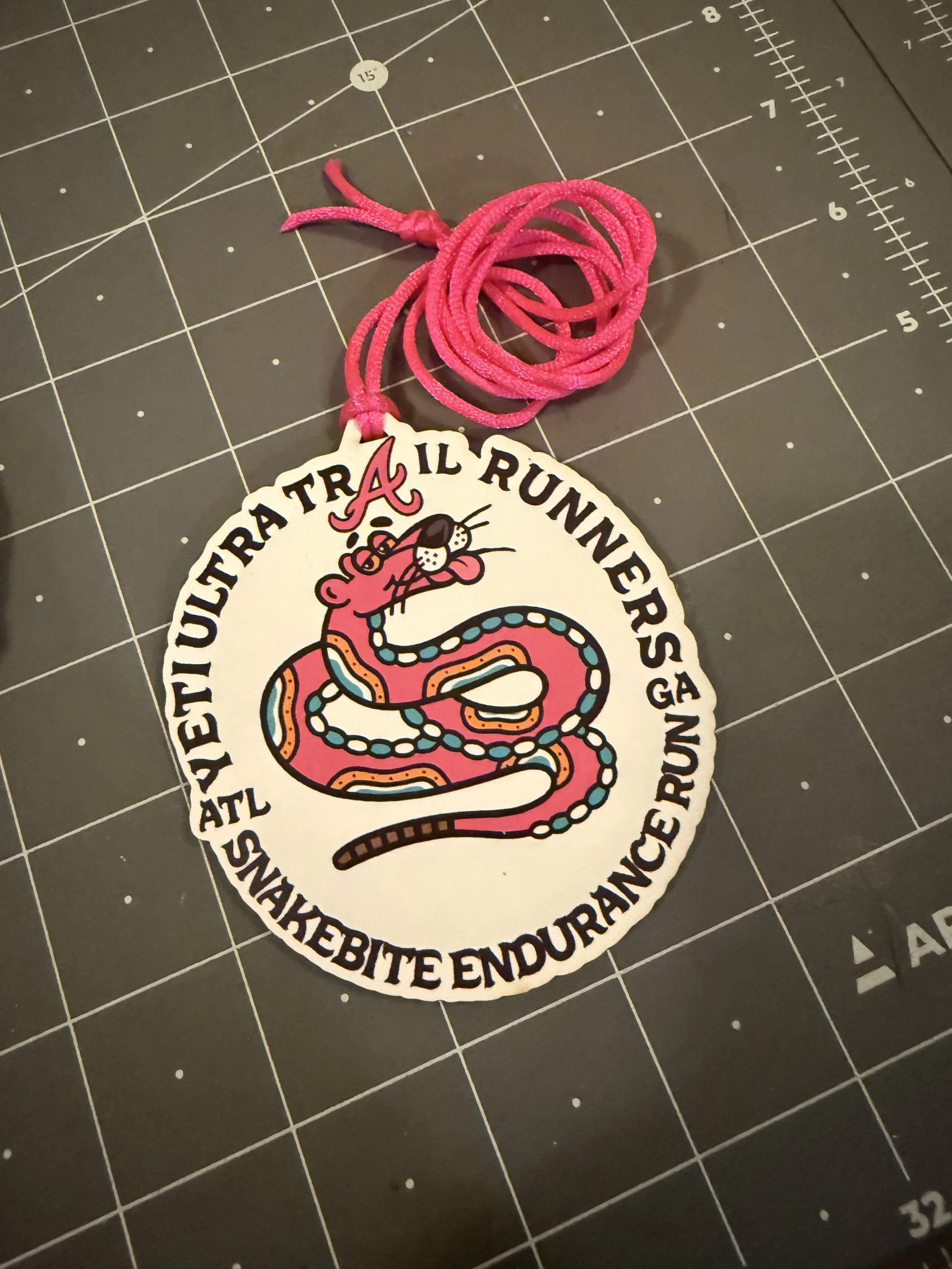 A colorful sticker with a pink snake and a pink mouse, featuring the text "AETIQUETUA TRA IL RUNNERSA ATL.SNAKEBITE ENDURANCE RUN" and a pink shoelace attached at the top.