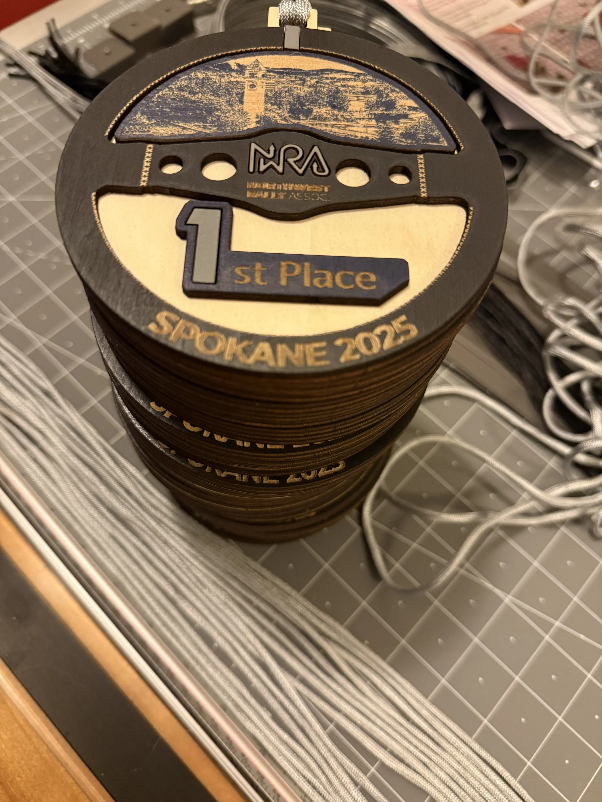Stack of medals for a fishing competition, with the top one showing first place, the event 'Spokane 2025', and an image of a lighthouse and water.