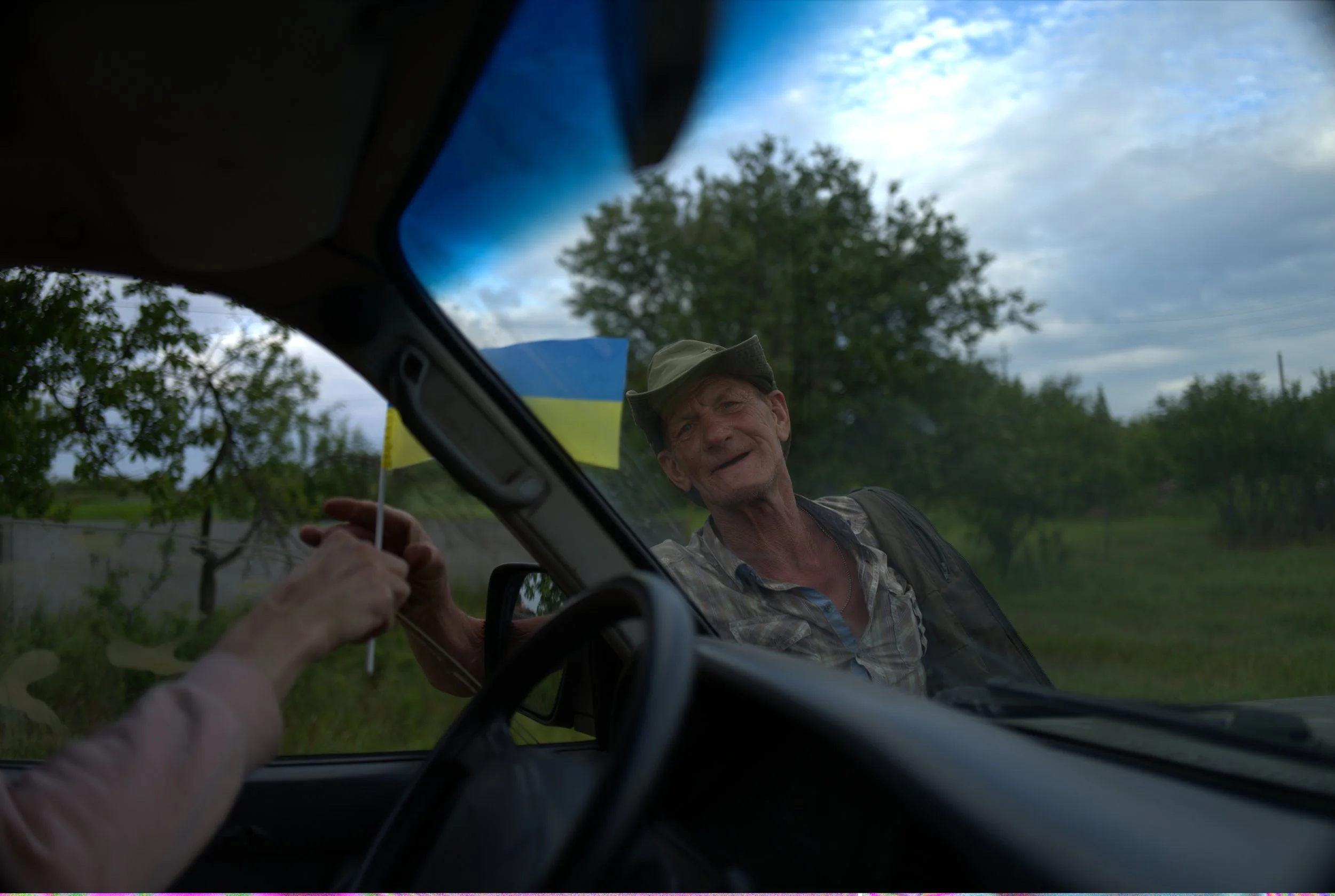 “A man handing a Ukrainian flag to a serviceman” by Kseniia Tomchyk