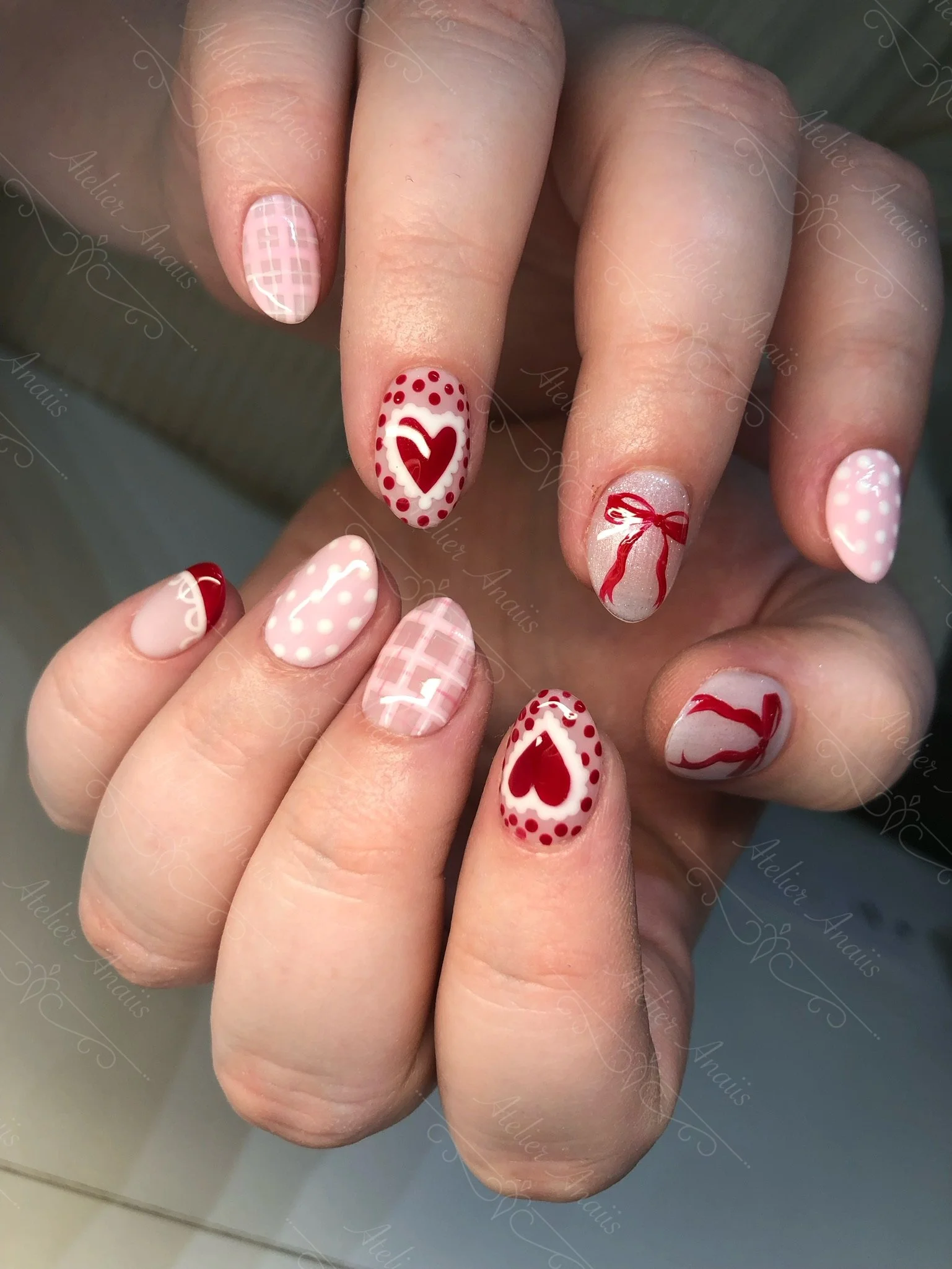 Medium nails featuring hand drawn red and white hearts and red bows nail art on soft pink base for Valentine’s Day.