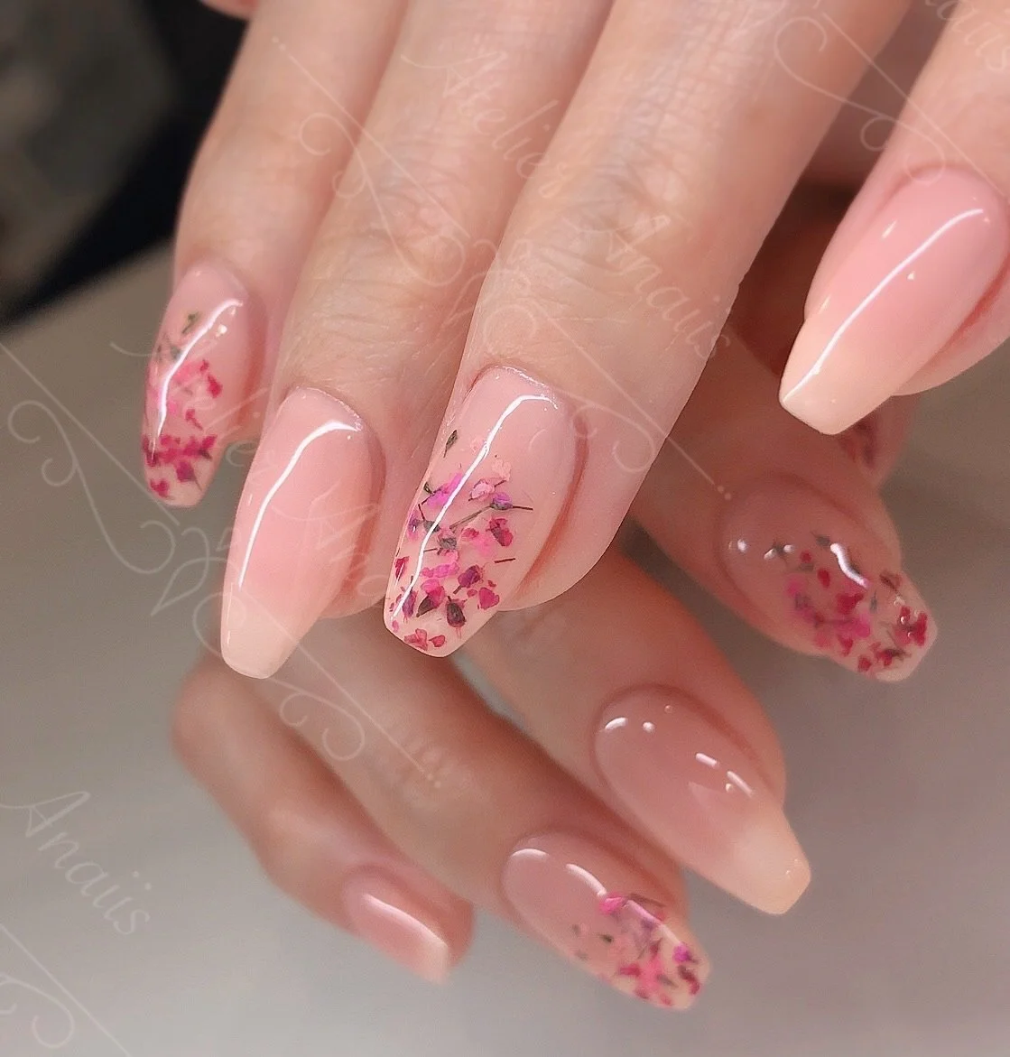 Hands with medium nails featuring hand drawn cherry blossom floral nail art on a glossy pink base for spring and summer.