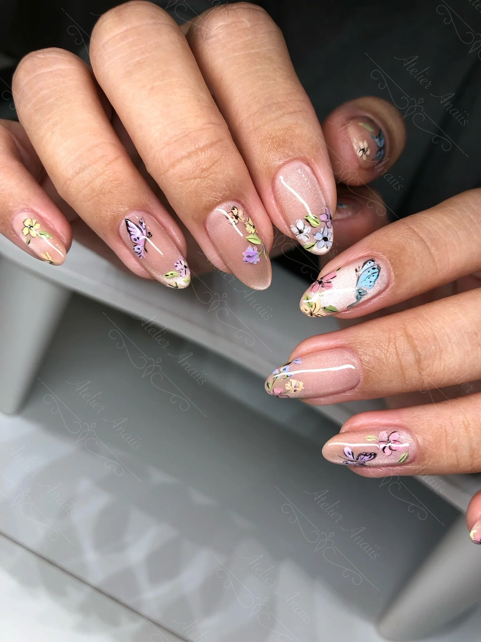 Hand with long nails featuring hand drawn butterflies and flowers on a nude cat-eye velvet base for spring and summer.