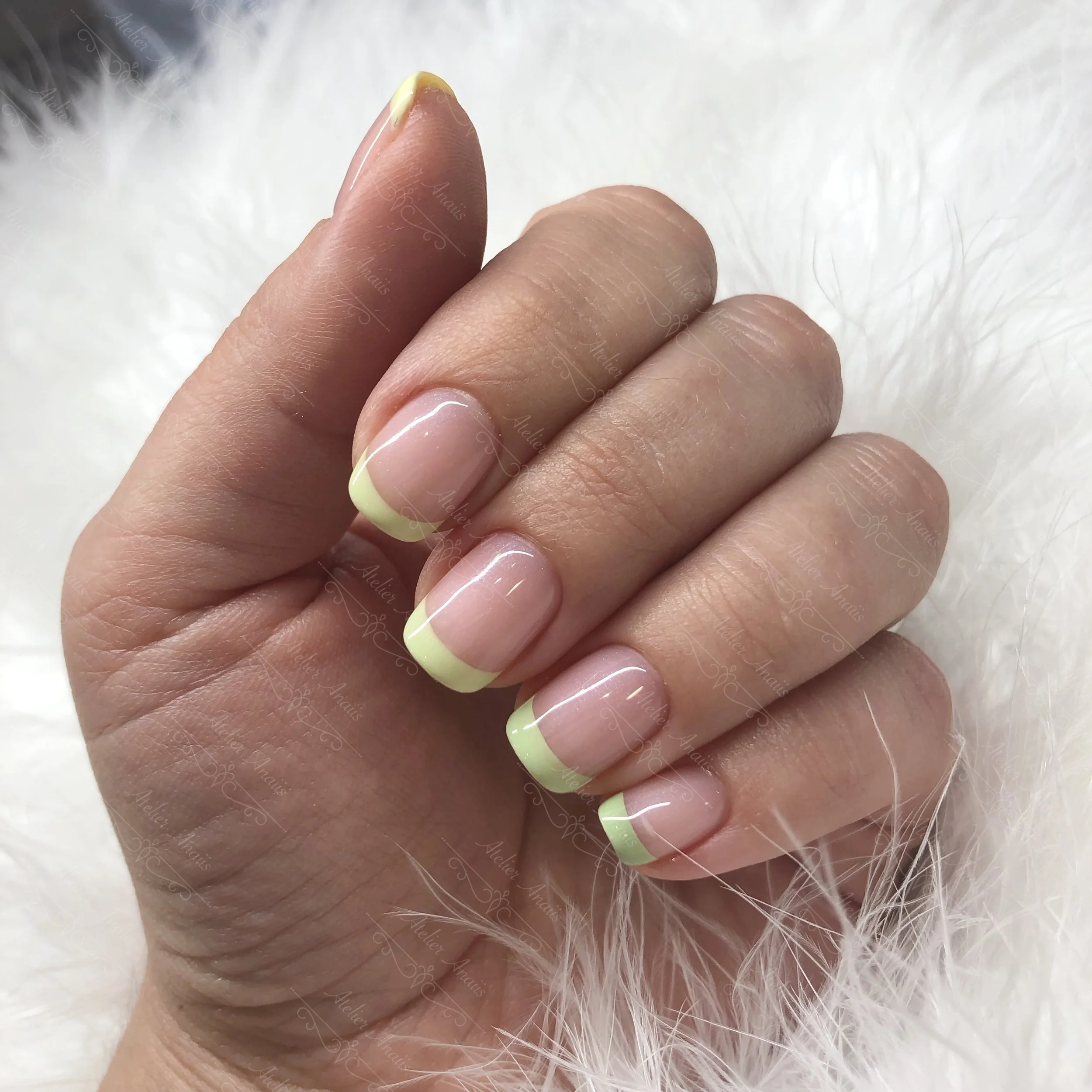 Hand with nails featuring lime green French tip nail art on nude base.