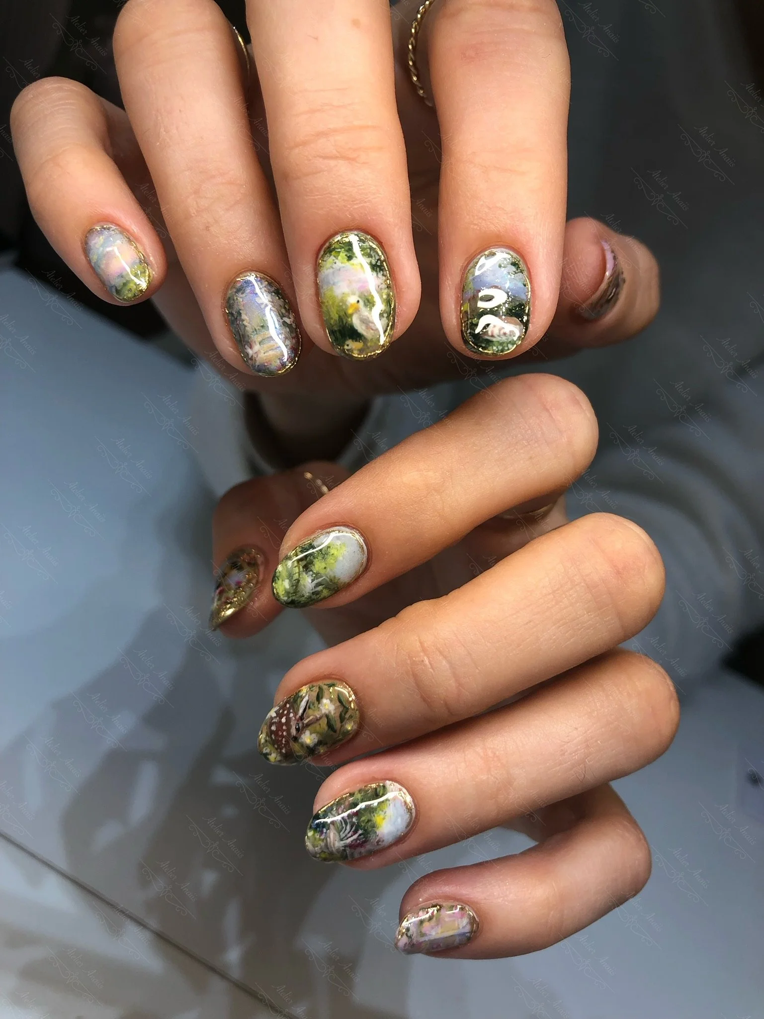 Hands with medium nails featuring hand drawn impressionist nail art with ducks and landscapes in green, yellow, and blue. 