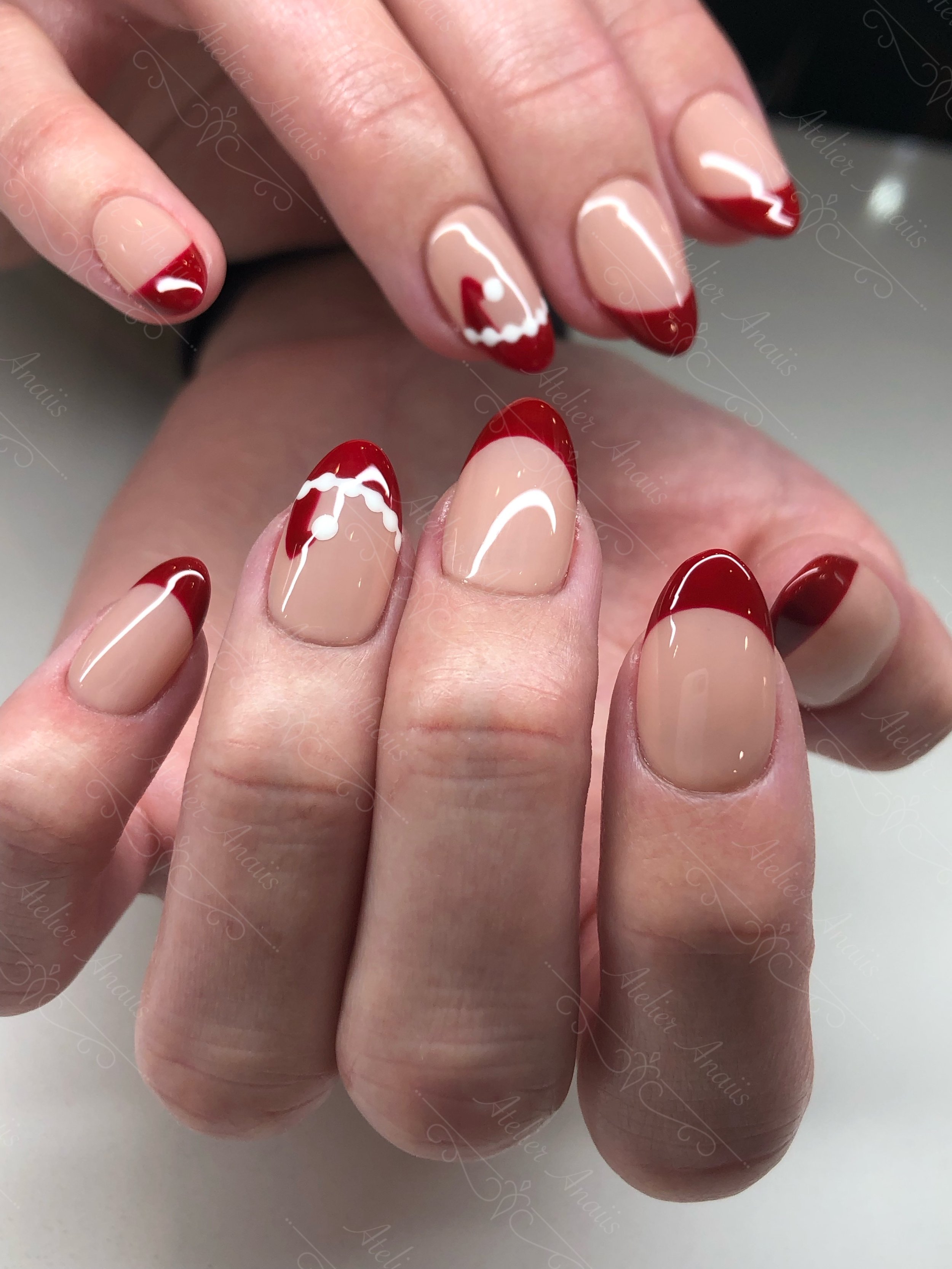 Medium nails featuring hand drawn santa hat and red French tip nail art on glossy nude base for Christmas.