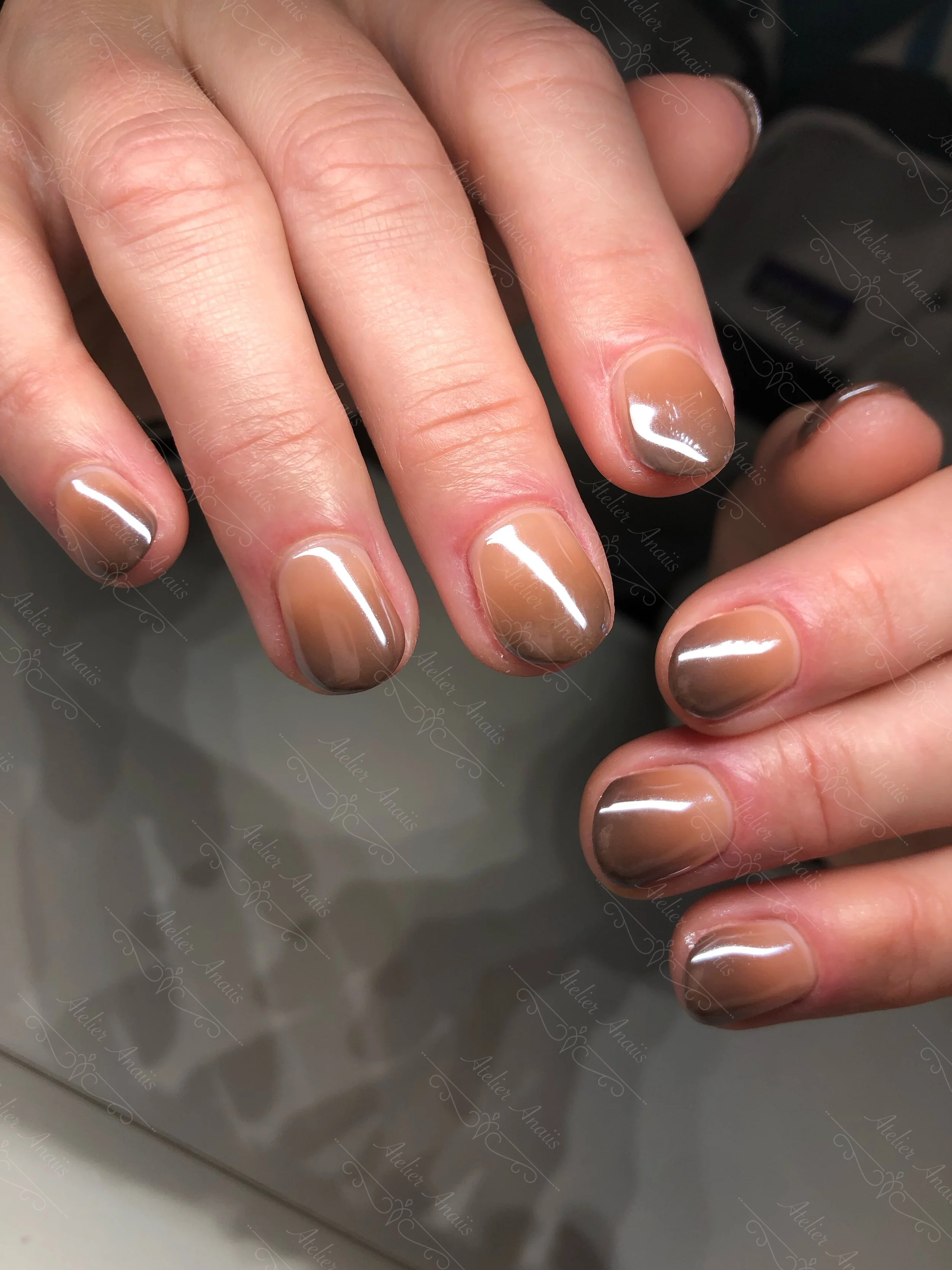 Hands with short natural nails featuring soft chestnut brown ombre nail art on a glossy nude base.