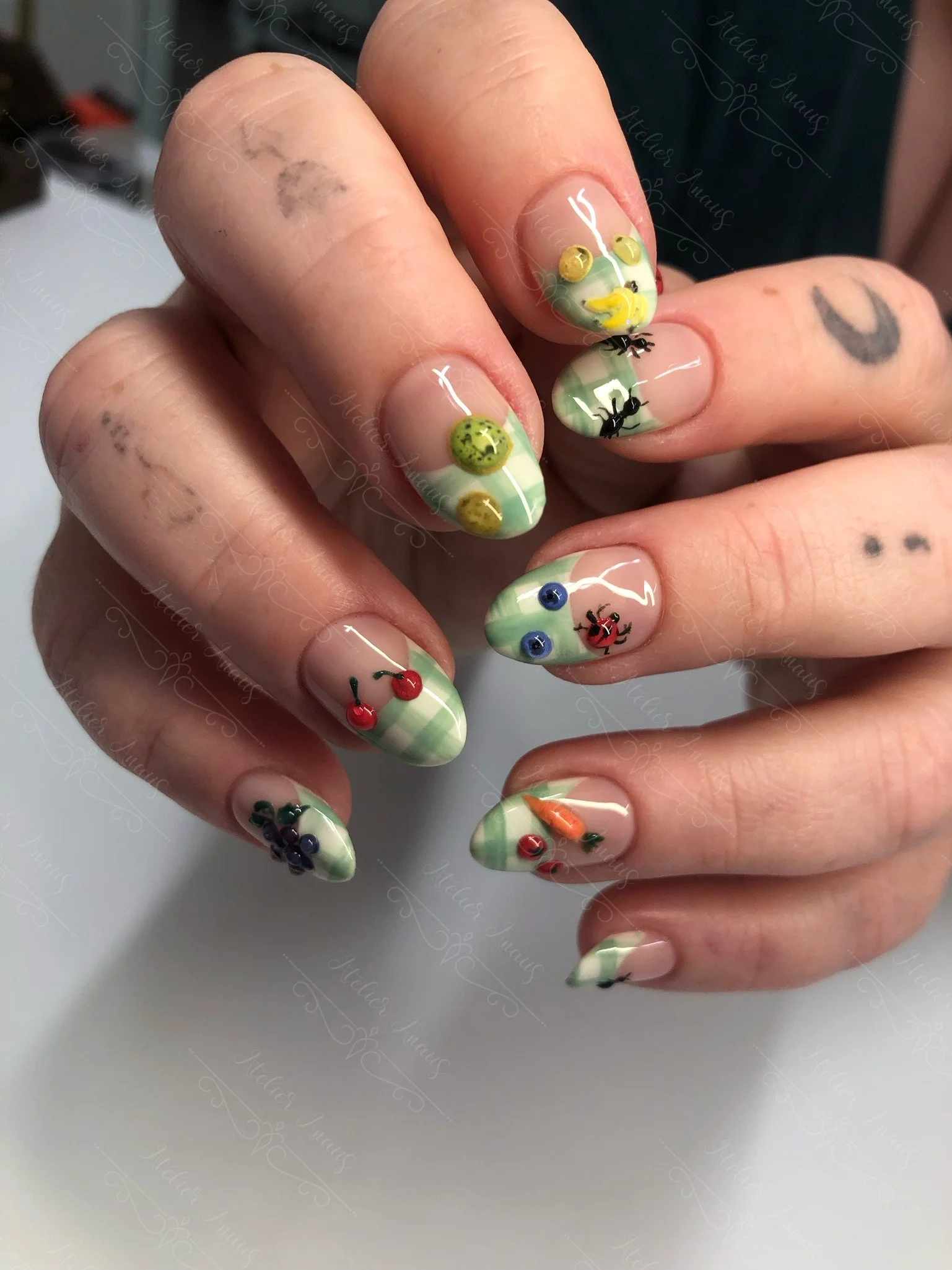 Hands with medium nails featuring hand drawn embossed 3d fruits and vegetables with light green french tip nail art on glossy nude base. 