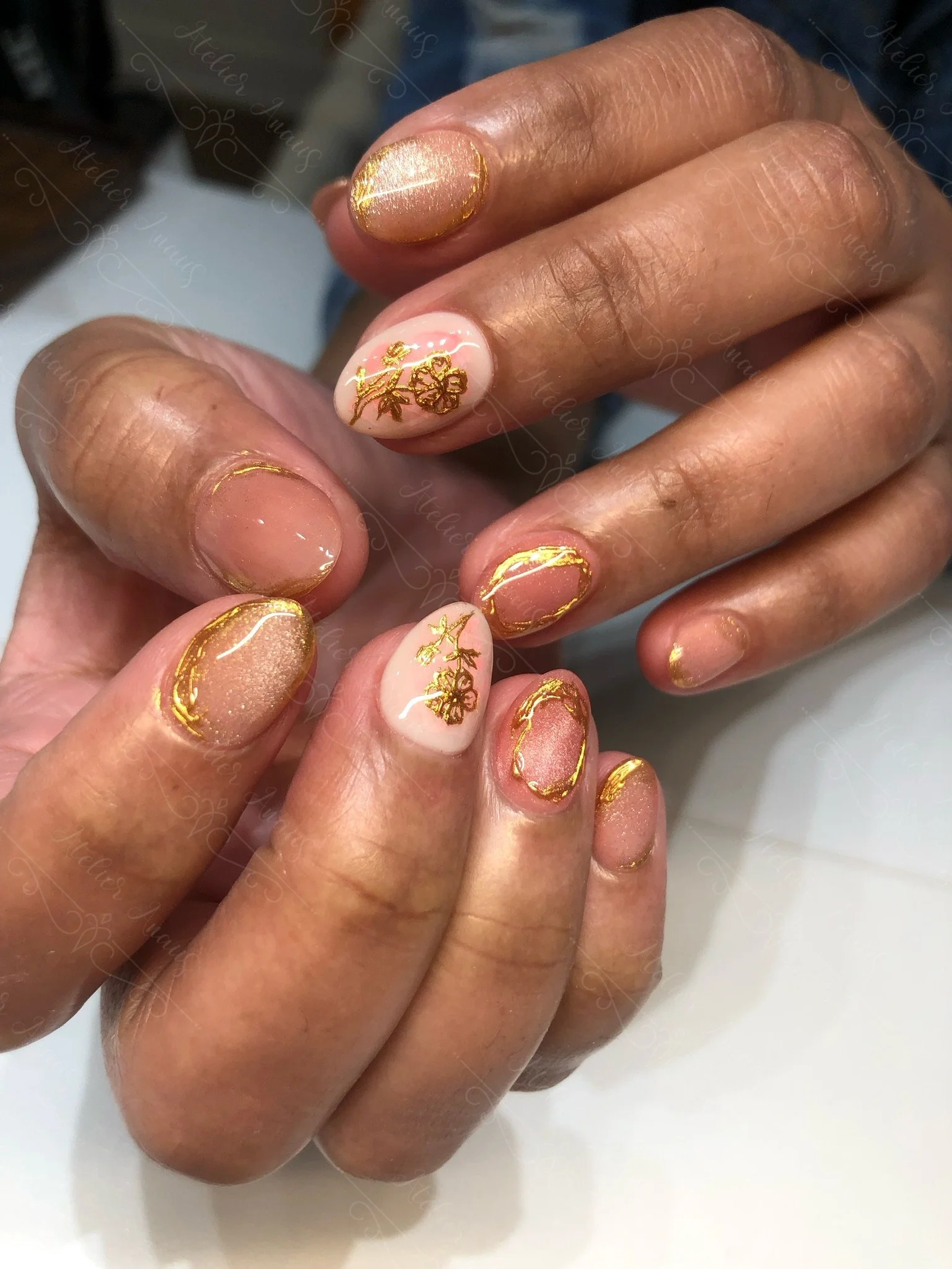 Hands with medium nails featuring hand drawn gold flower nail art on a glossy brown nude base. 