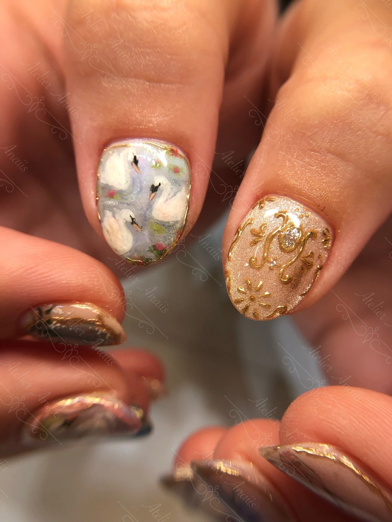 Hands with medium thumb nails featuring hand drawn impressionist nail art inspired by Swan Lake with white swans and gold leaf. 