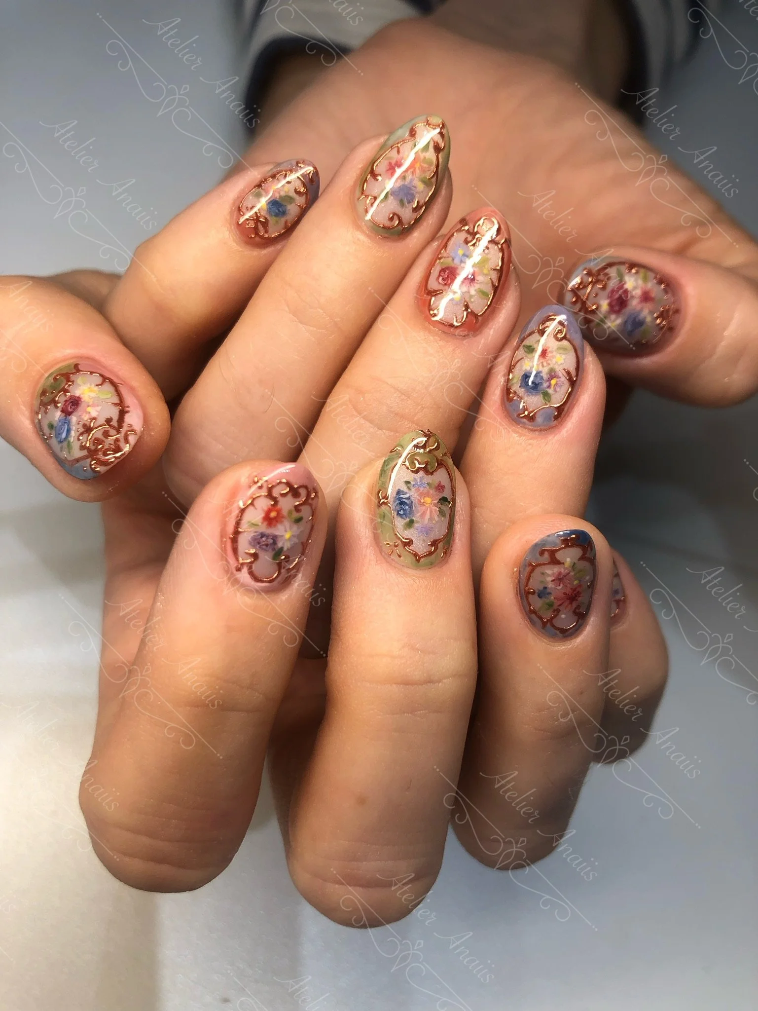 Hands with medium nails featuring hand drawn impressionist nail art inspired by grand frames of paintings in red, gold, and blue. 