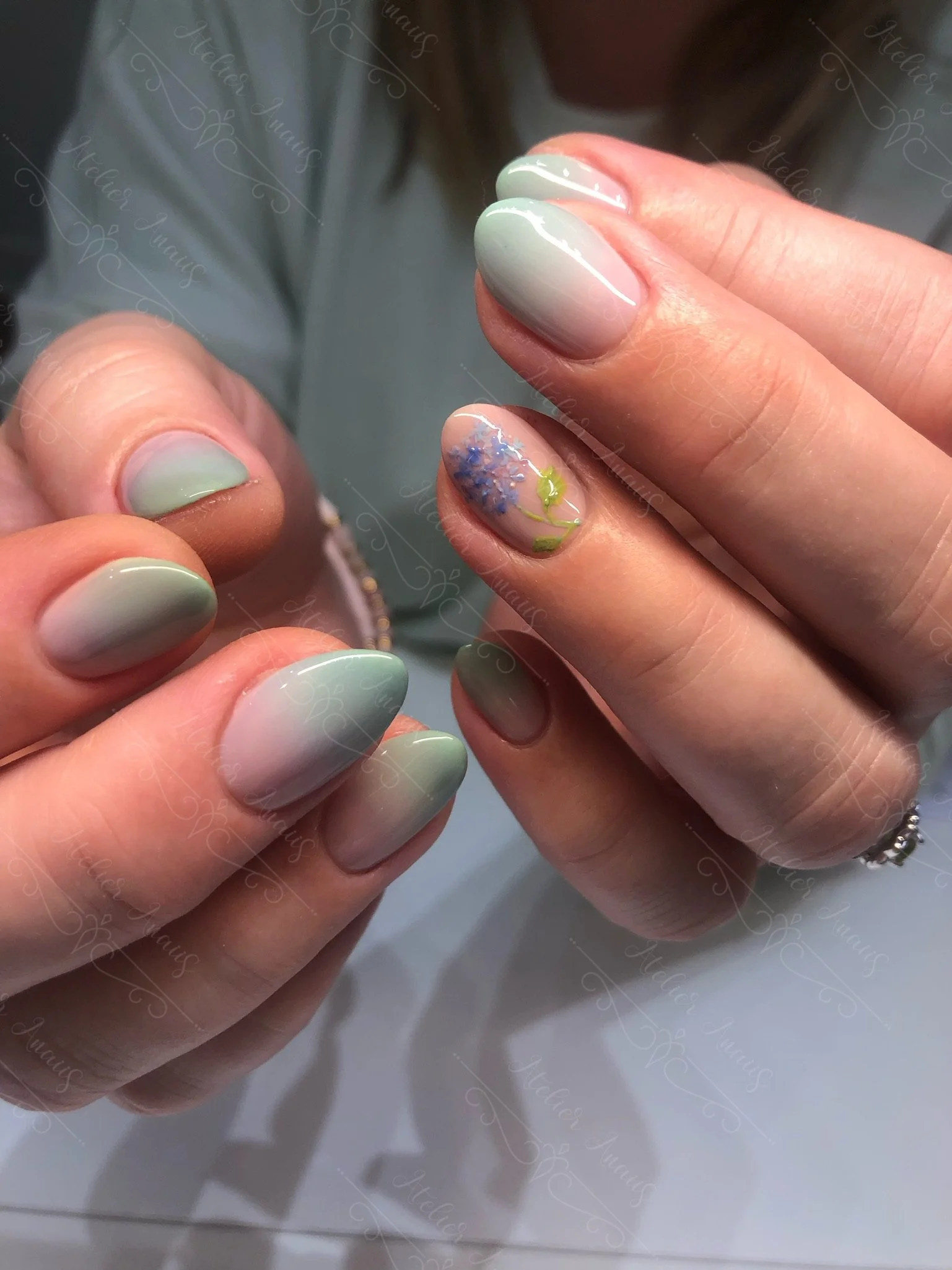 Hands with medium nails featuring hand drawn purple flower nail art on a pastel green ombre base for spring and summer.