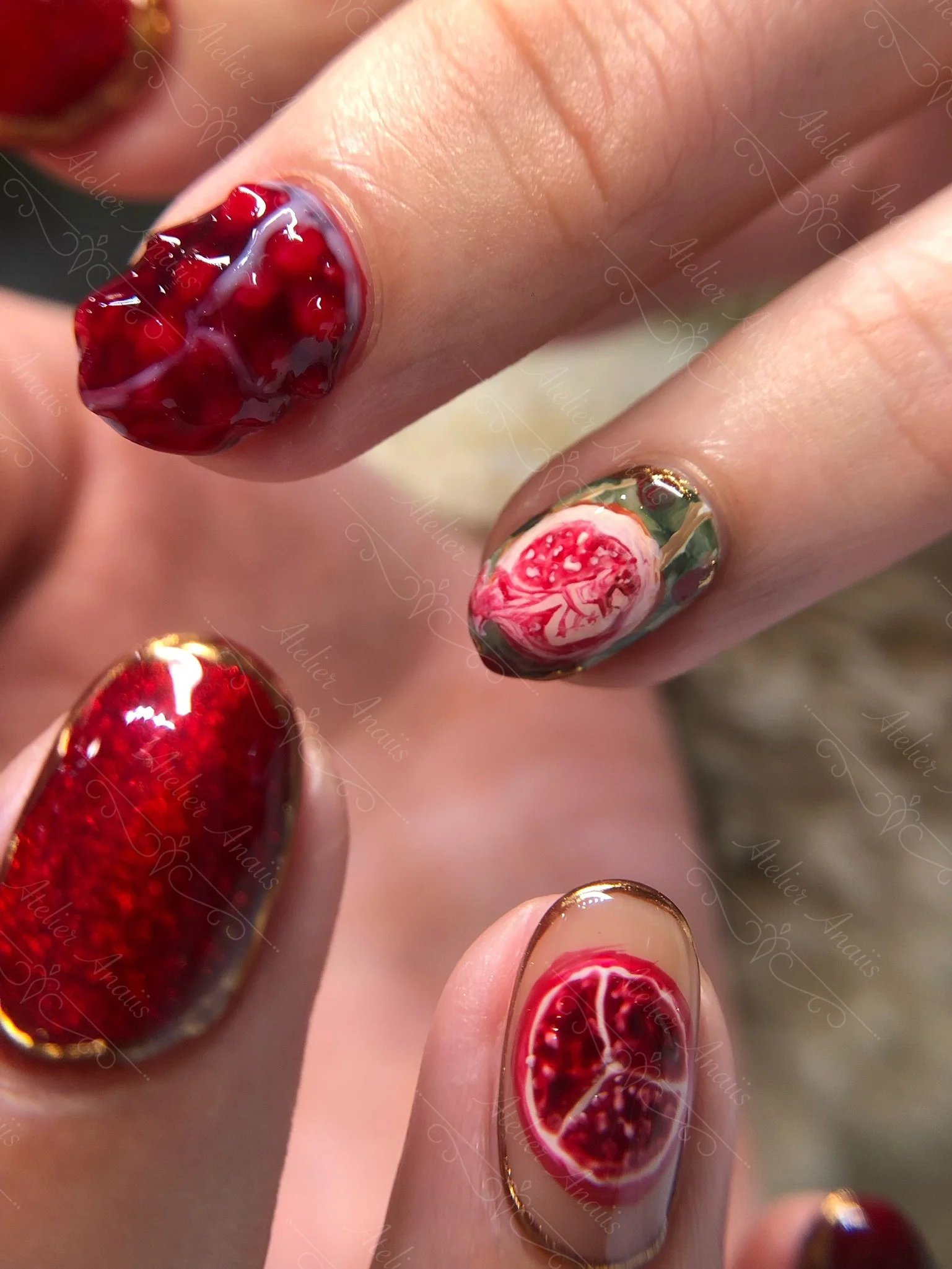 Hands with short natural nails featuring hand drawn embossed 3d pomegranates nail art on red cat-eye velvet base for summer. 
