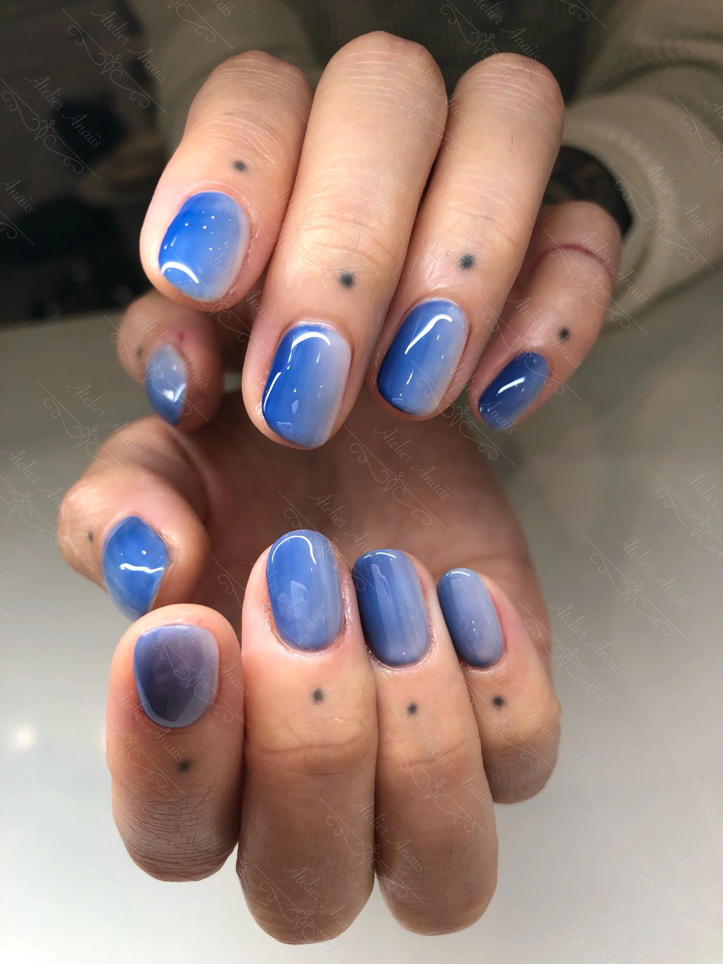 Hands with short nails featuring vertical blue ombre nail art.
