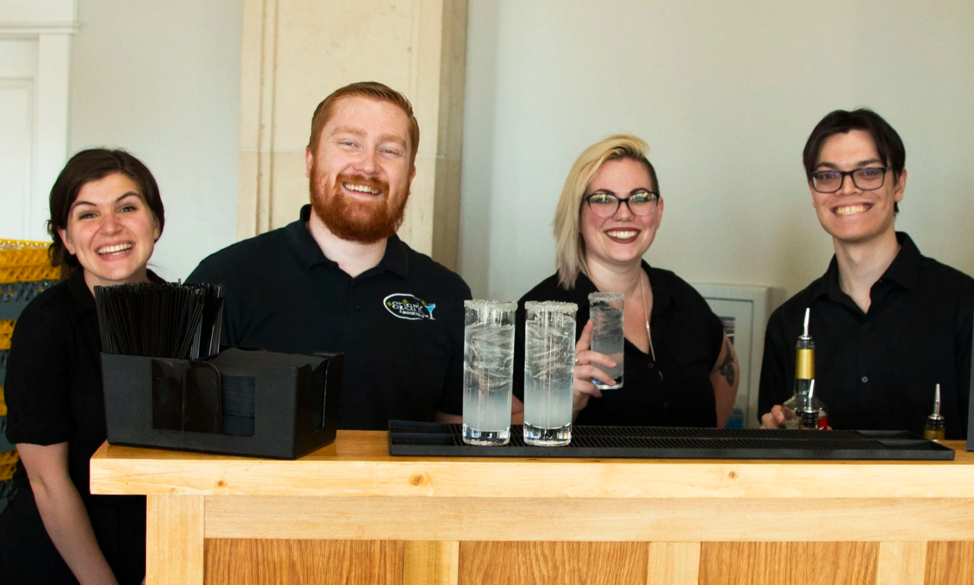Four bar staff standing behind a bar counter, smiling.
