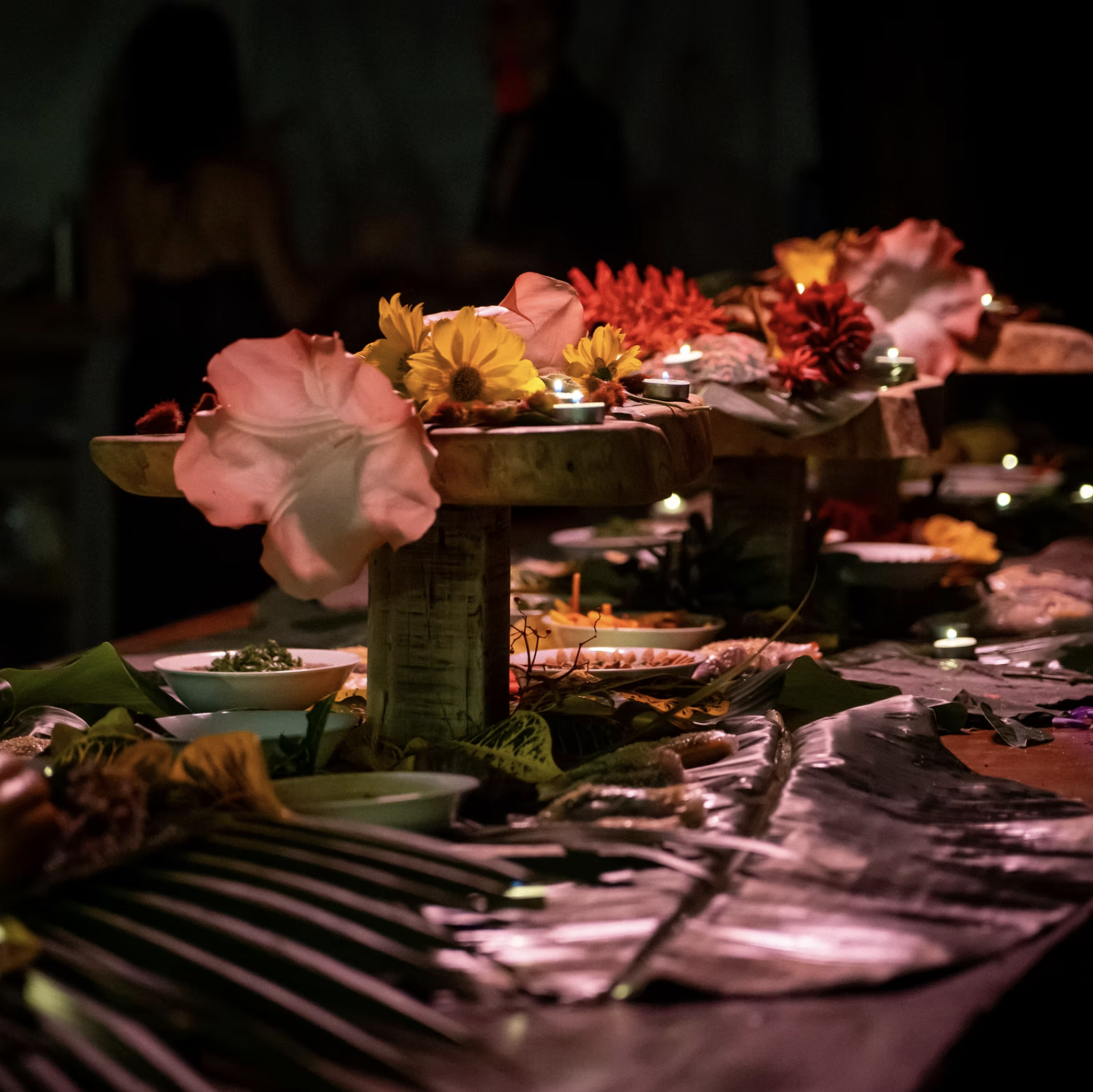 A table decorated with flowers, candles, and food in low lighting, likely at a celebration or event.
