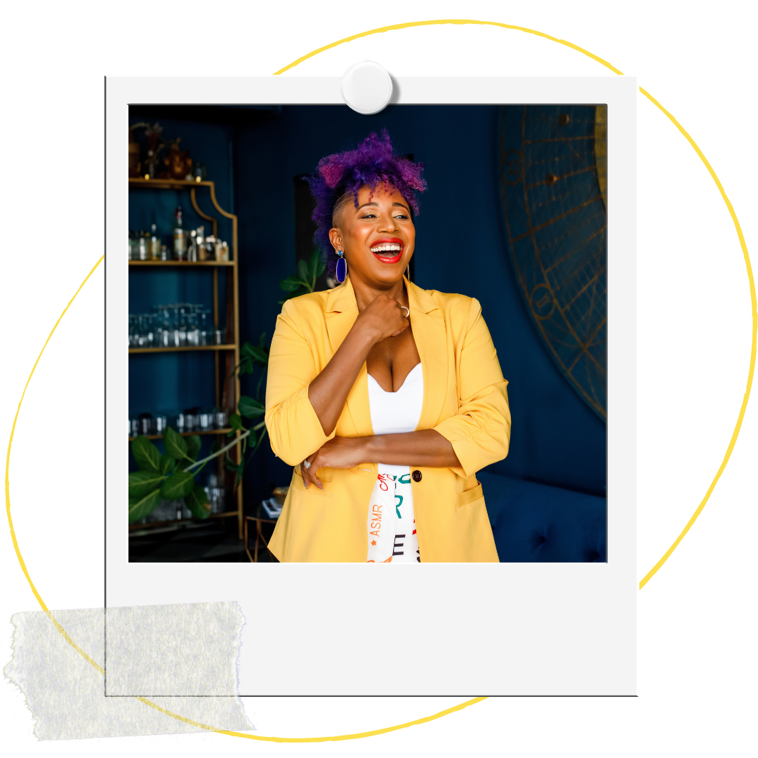 A woman, Dr. Mel Robinson-Brown, with purple and pink hair, wearing a yellow blazer and white top, smiling and laughing indoors.