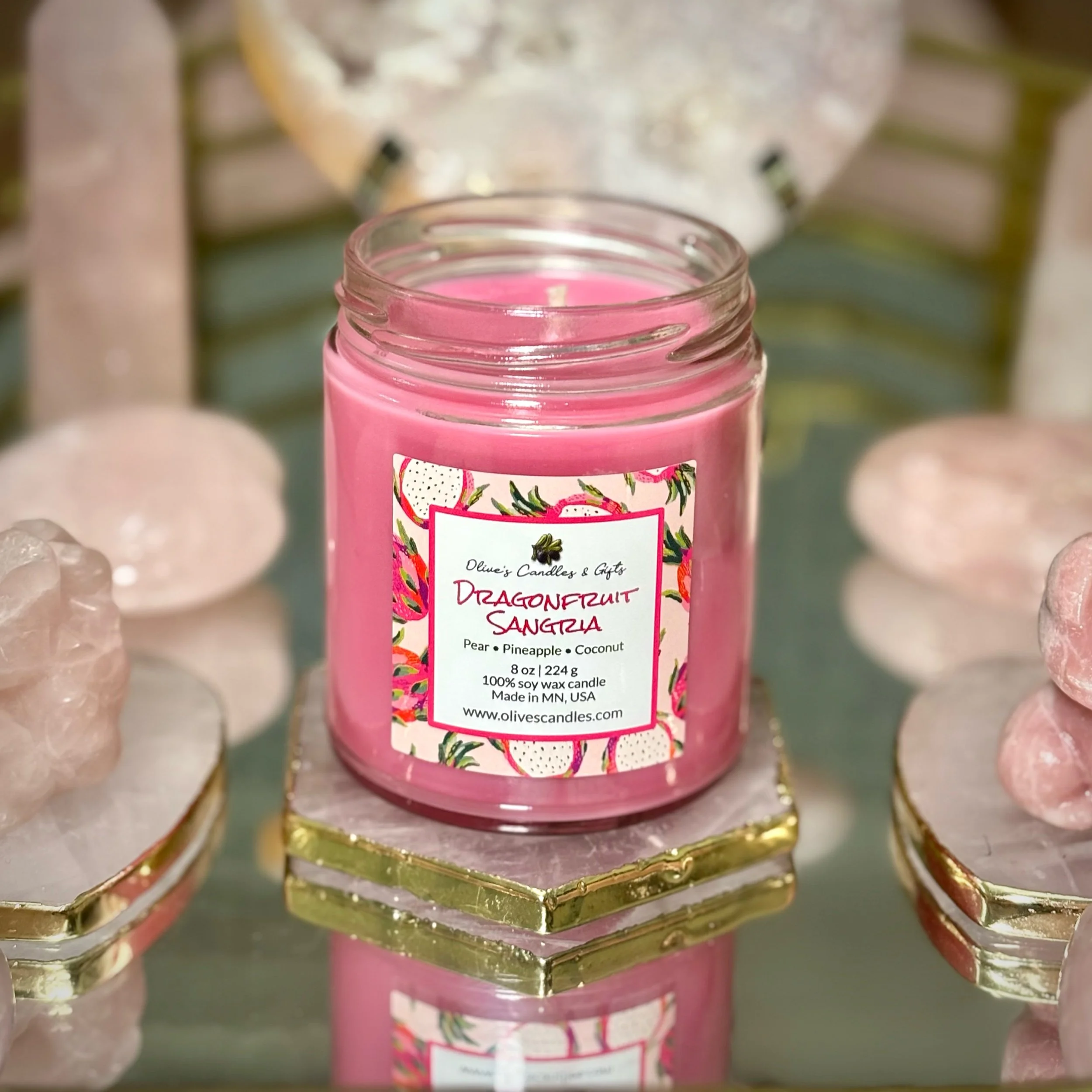 Pink dragonfruit sangria soy wax candle in a clear jar on top of a gold rimmed rose quartz crystal slab surrounded by rose quartz crystal hearts