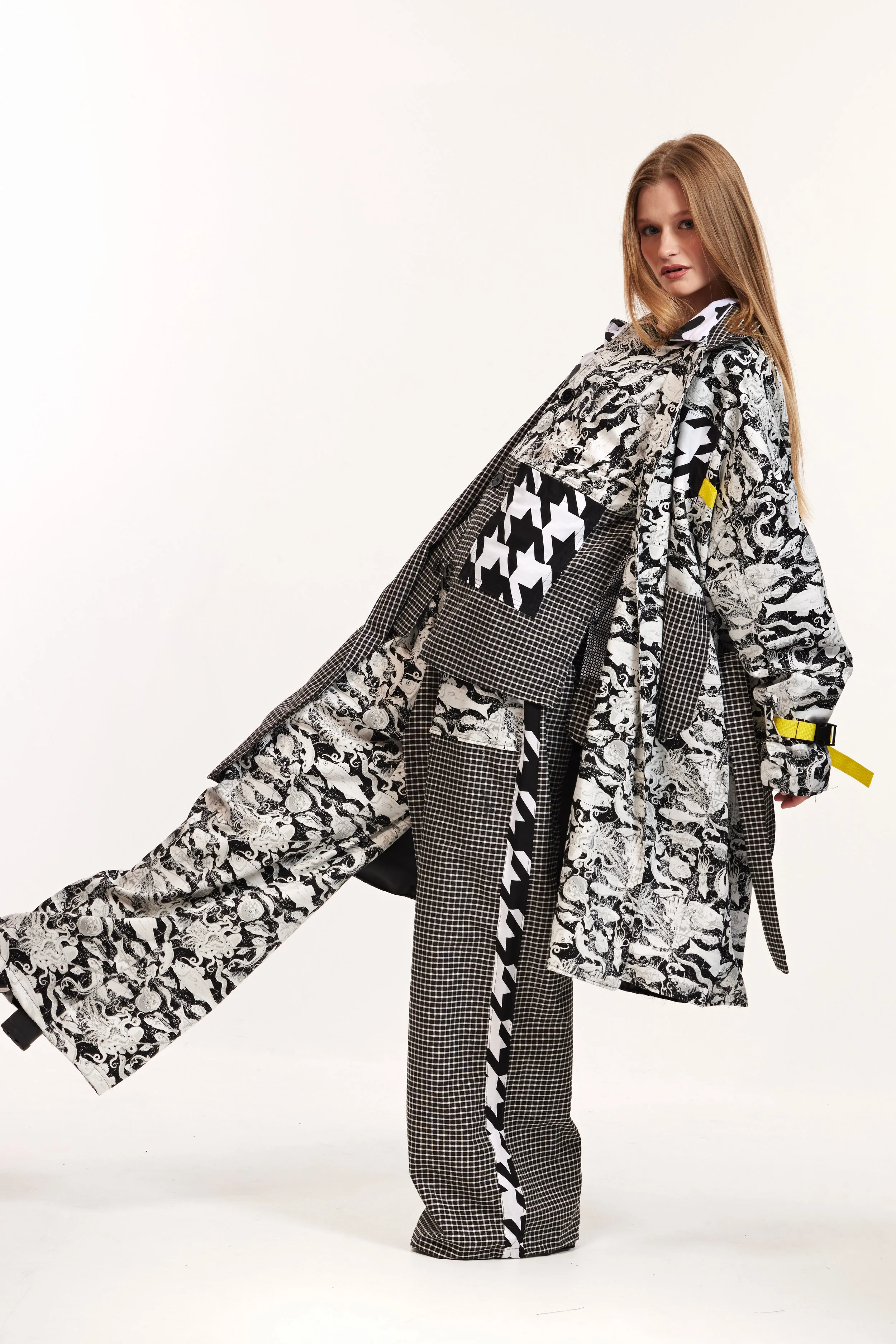 Fashion model wearing a black-and-white patterned oversized jacket and matching checkered pants against a white background