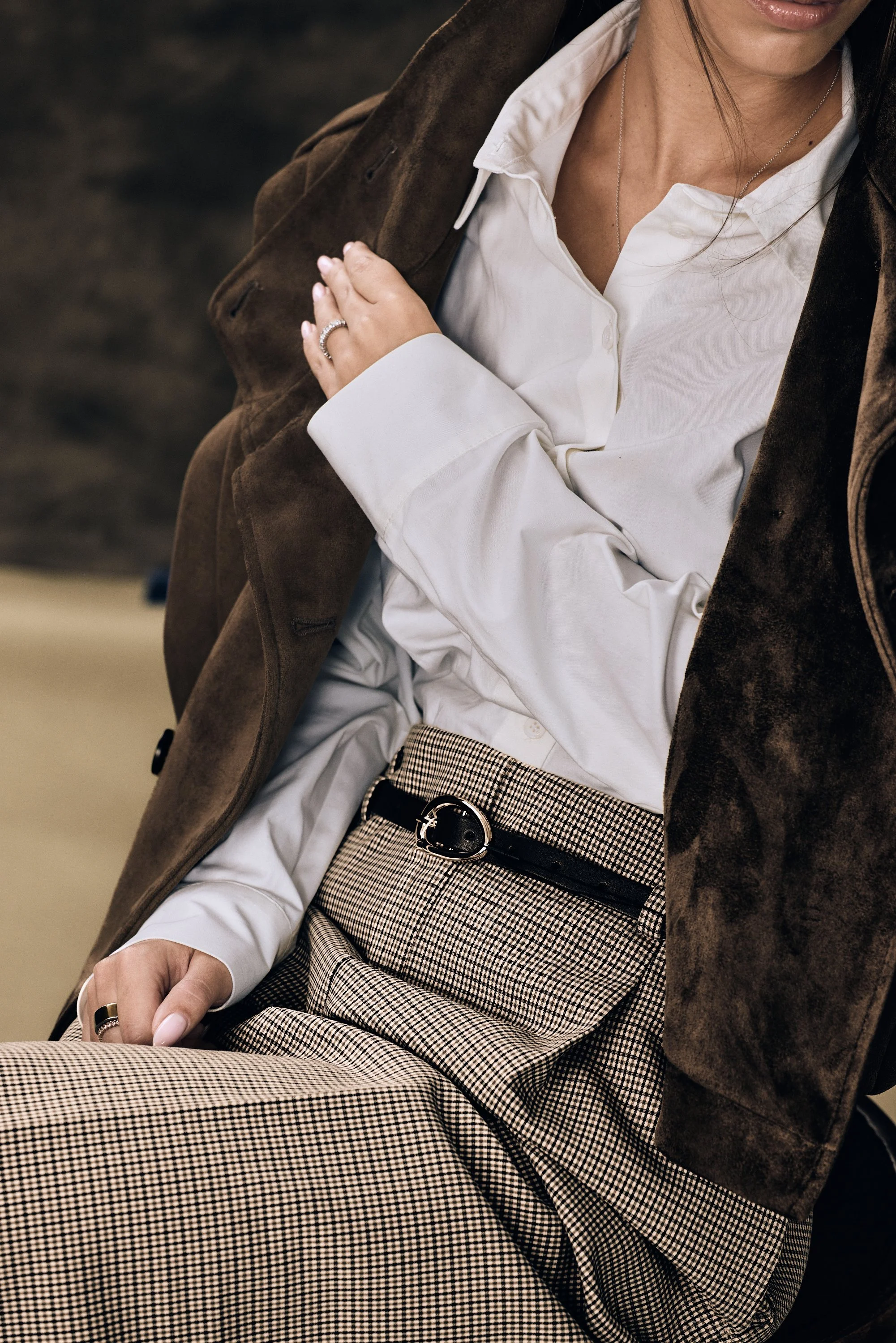 Close-up of a woman wearing a white blouse, brown coat, houndstooth skirt, belt, and jewelry