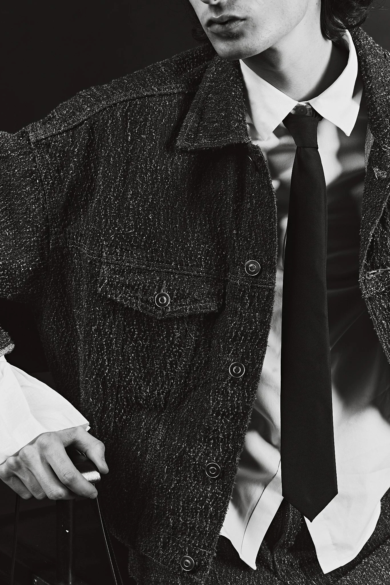 Black-and-white close-up of a person wearing a textured dark coat over a white dress shirt and black tie