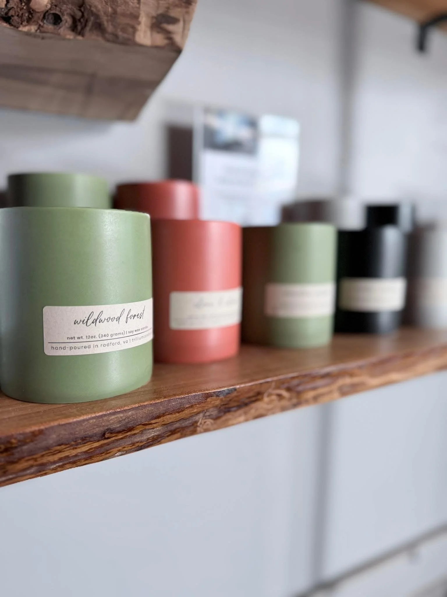 Close-up of rolled candles in green, red, beige, and black colors on a rustic wooden shelf.