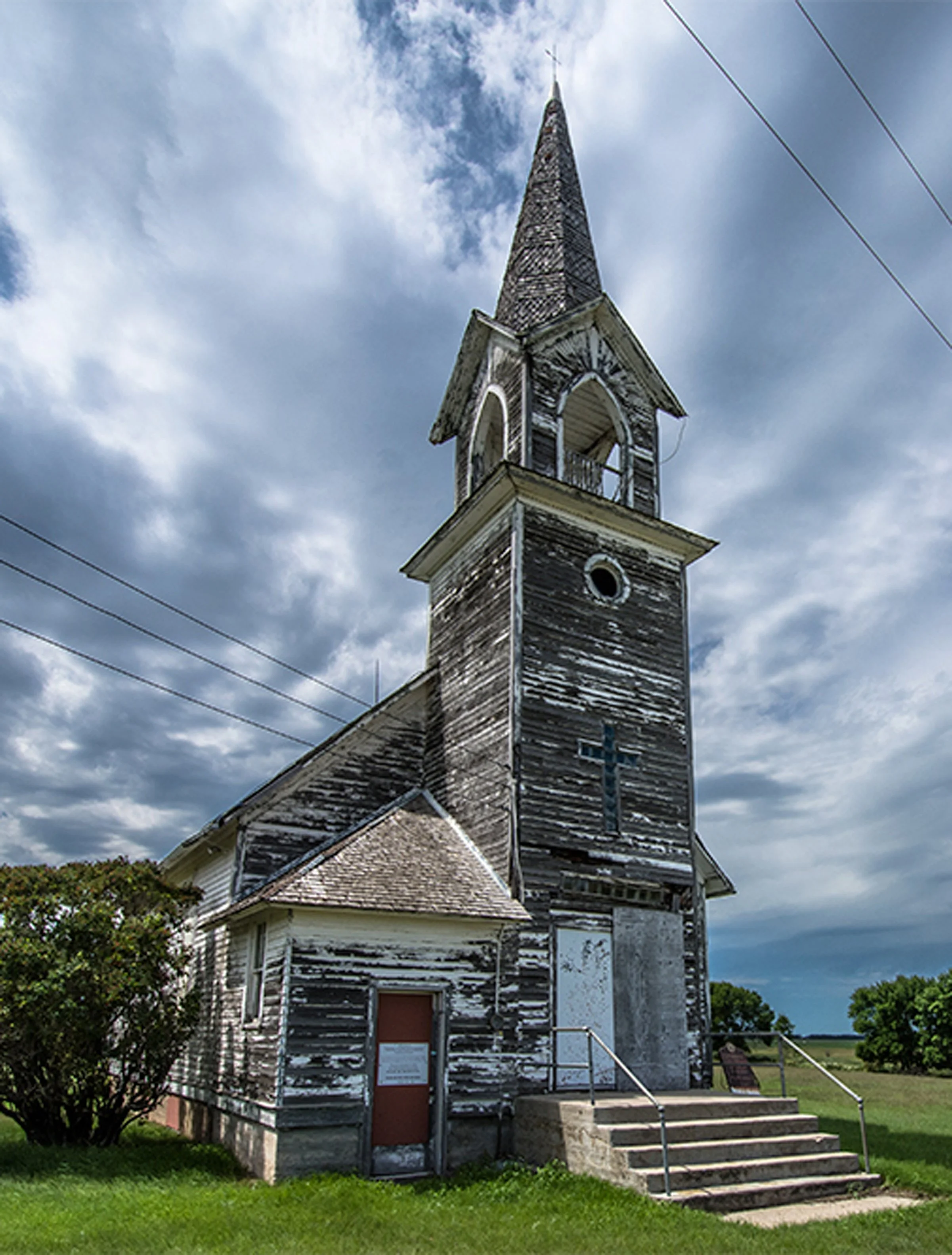 Tunbridge Lutheran Church with black weathered paint, surrounded by a grassy church grounds and under a partly cloudy sky.