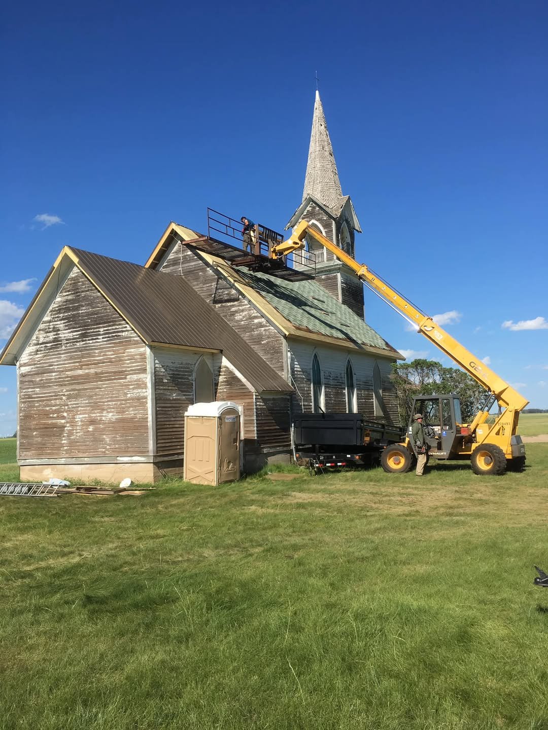 Workers using a forklift to repair the roof of Tunbridge Lutheran Church on a sunny day.