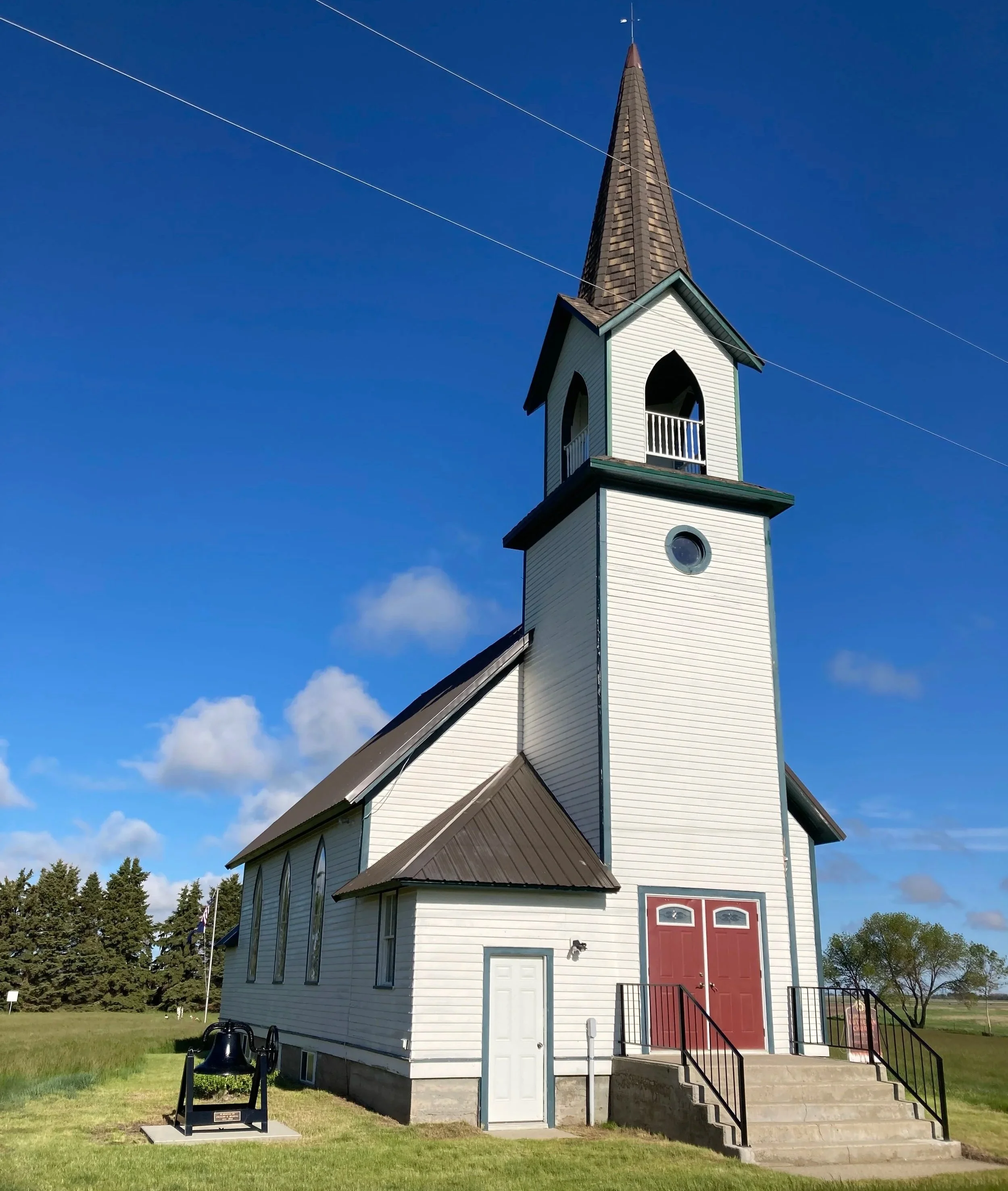 Renovated Tunbridge Lutheran Church with grounds and trees in the background, under a partly cloudy blue sky.