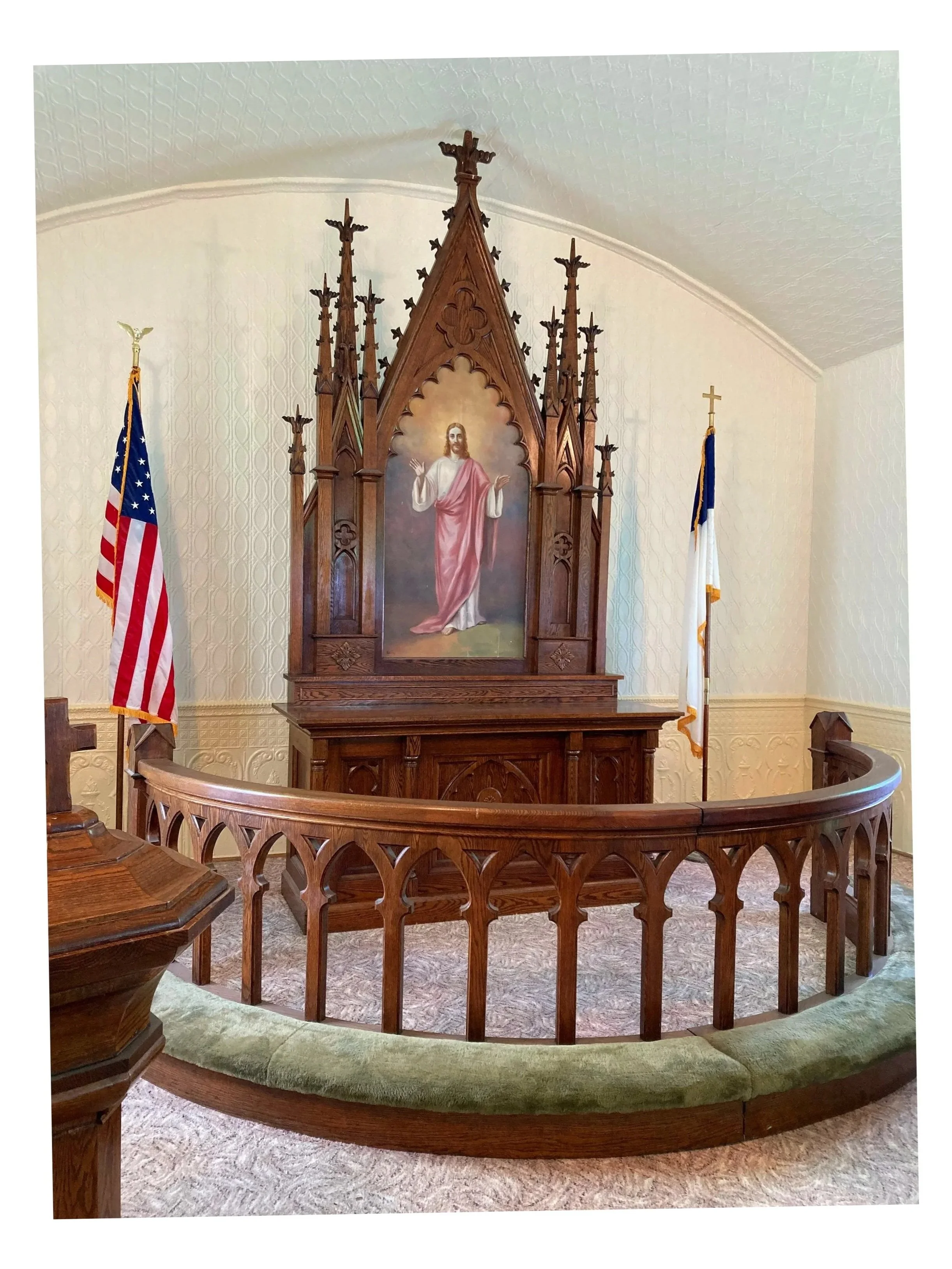 Altar space of Tunbridge Lutheran Church after walls were repainted white. Altar features a painting of Jesus Christ with open arms, flanked by two American flags, and a green-carpeted semicircular railing.