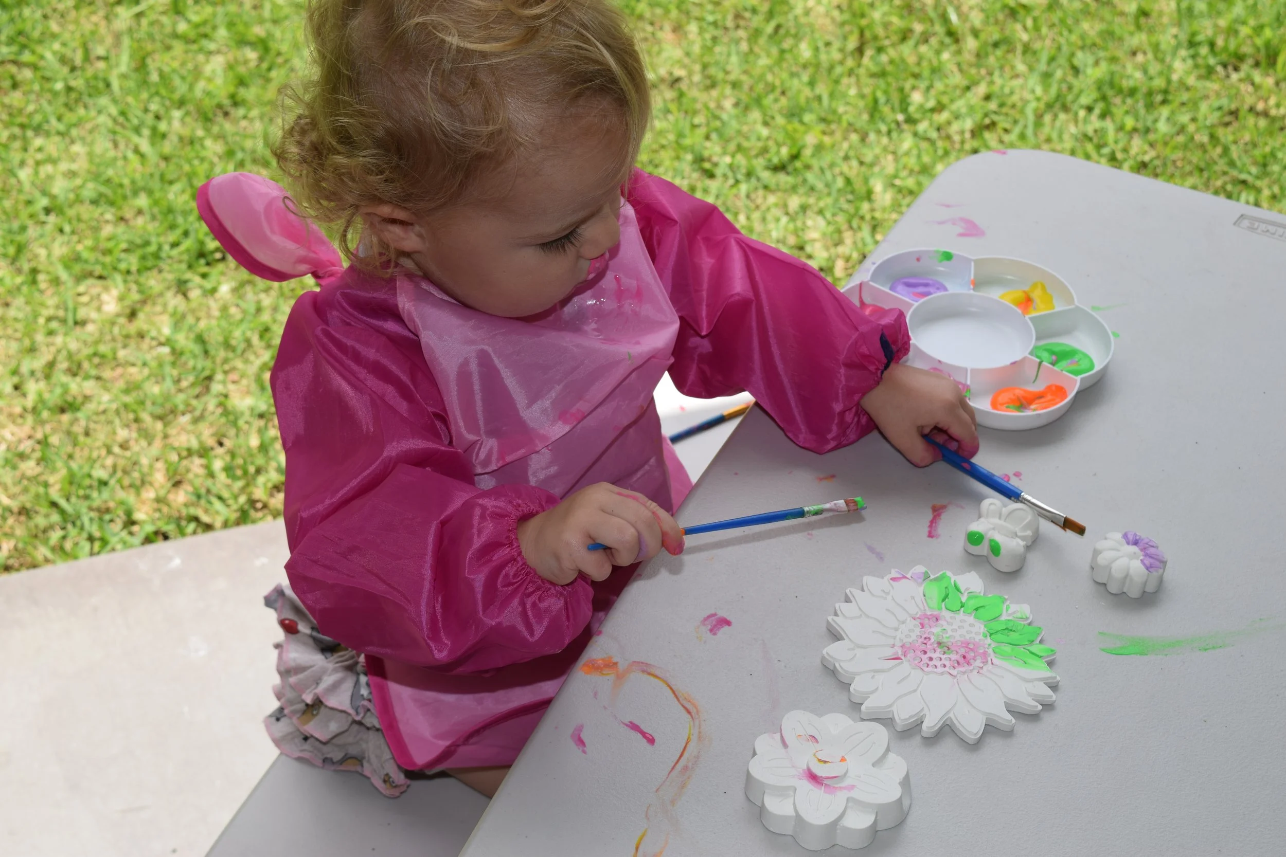 Little girl painting plaster flower molds at a table with a paint palette next to her.