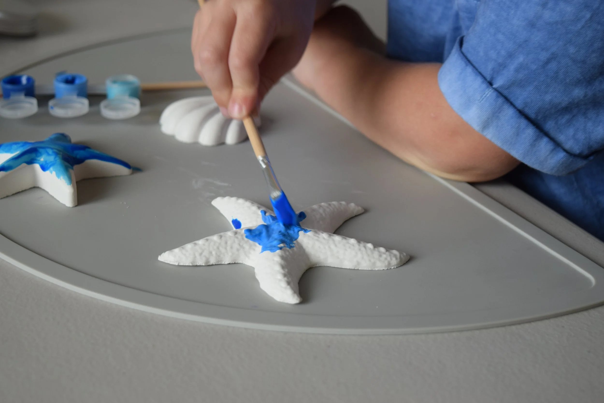 Child painting a plaster starfish with blue paint