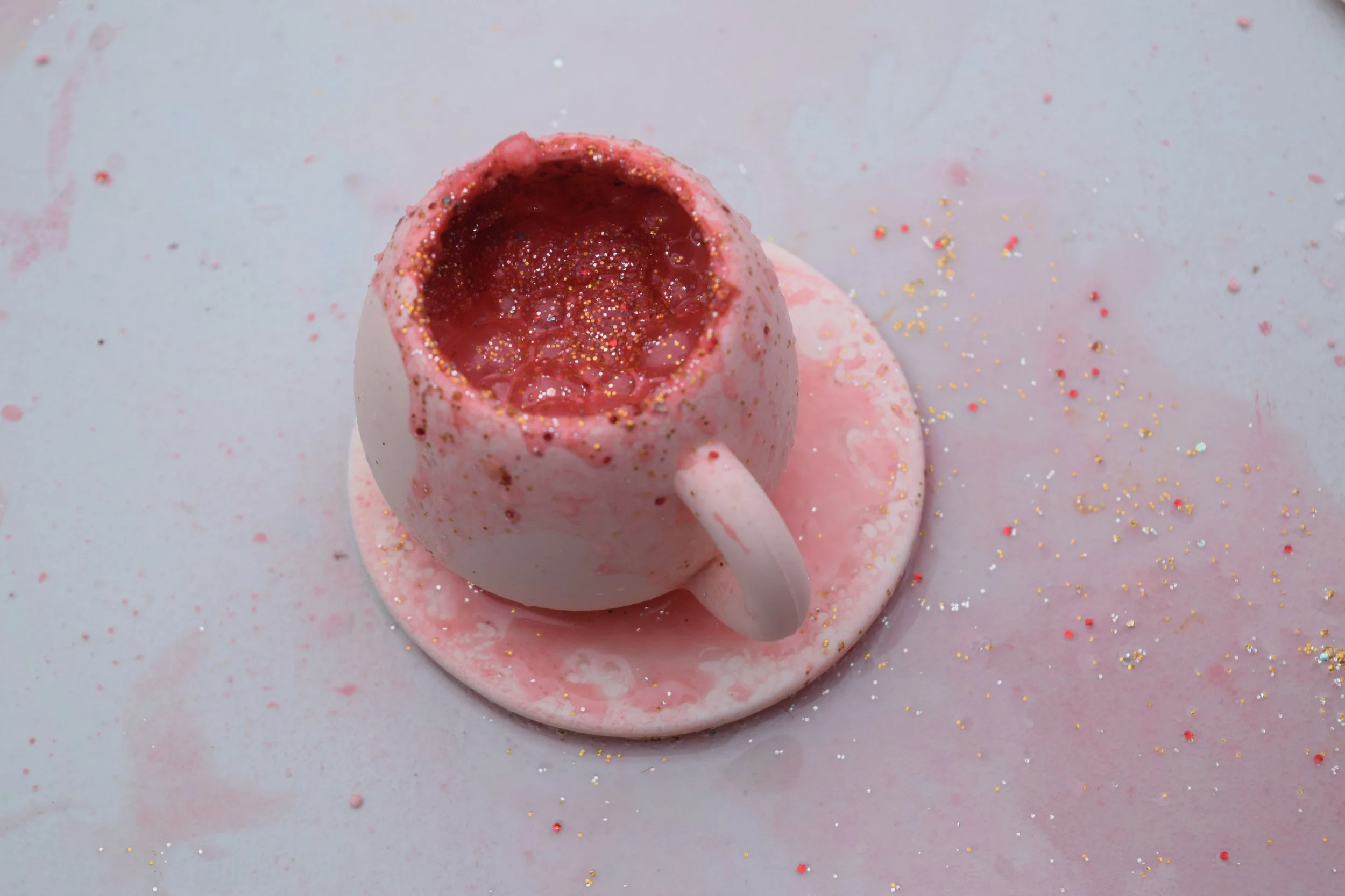 Pink cappuccino mug with frothy pink potion and gold glitter on saucer.