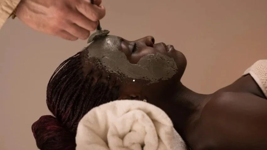 A woman lying with her eyes closed as a facial mask is being applied to her face in a spa setting.