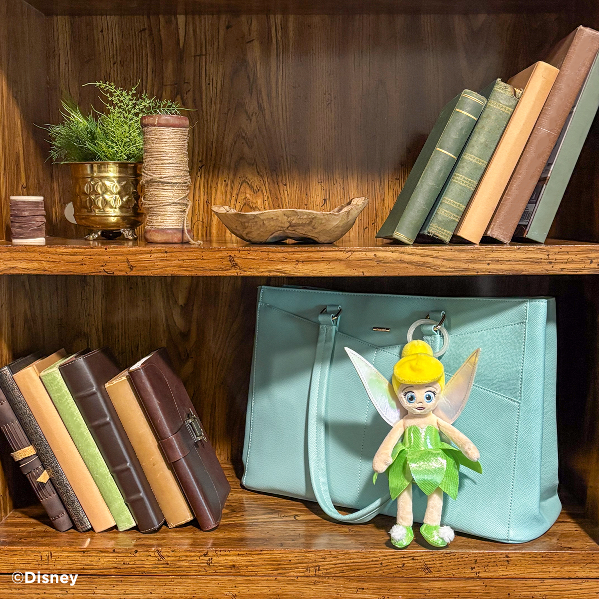 Disney Tinker Bell Scentsy Buddy Clip attached to a handbag on a bookshelf with books and decor