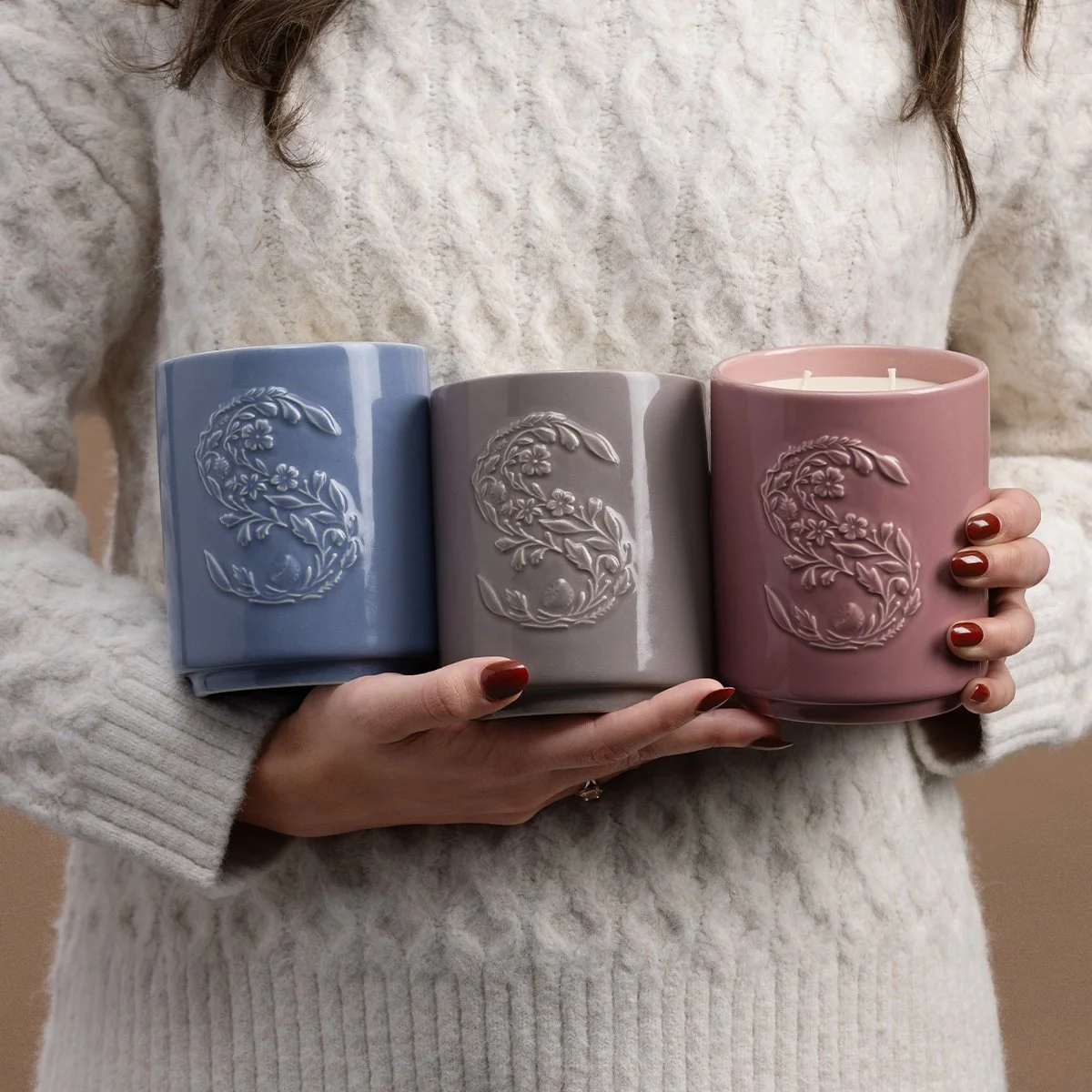 Woman holding three Scentsy candles in different colours, including Cashmere Vanilla Sugar, in a lifestyle setting
