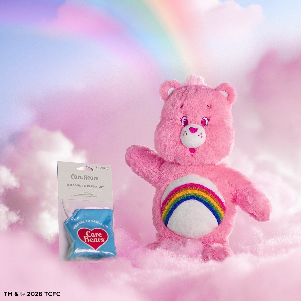 Care Bears Cheer Bear Scentsy Buddy plush with rainbow belly badge displayed with Welcome to Care-A-Lot Scent Pak in a soft pastel cloud background