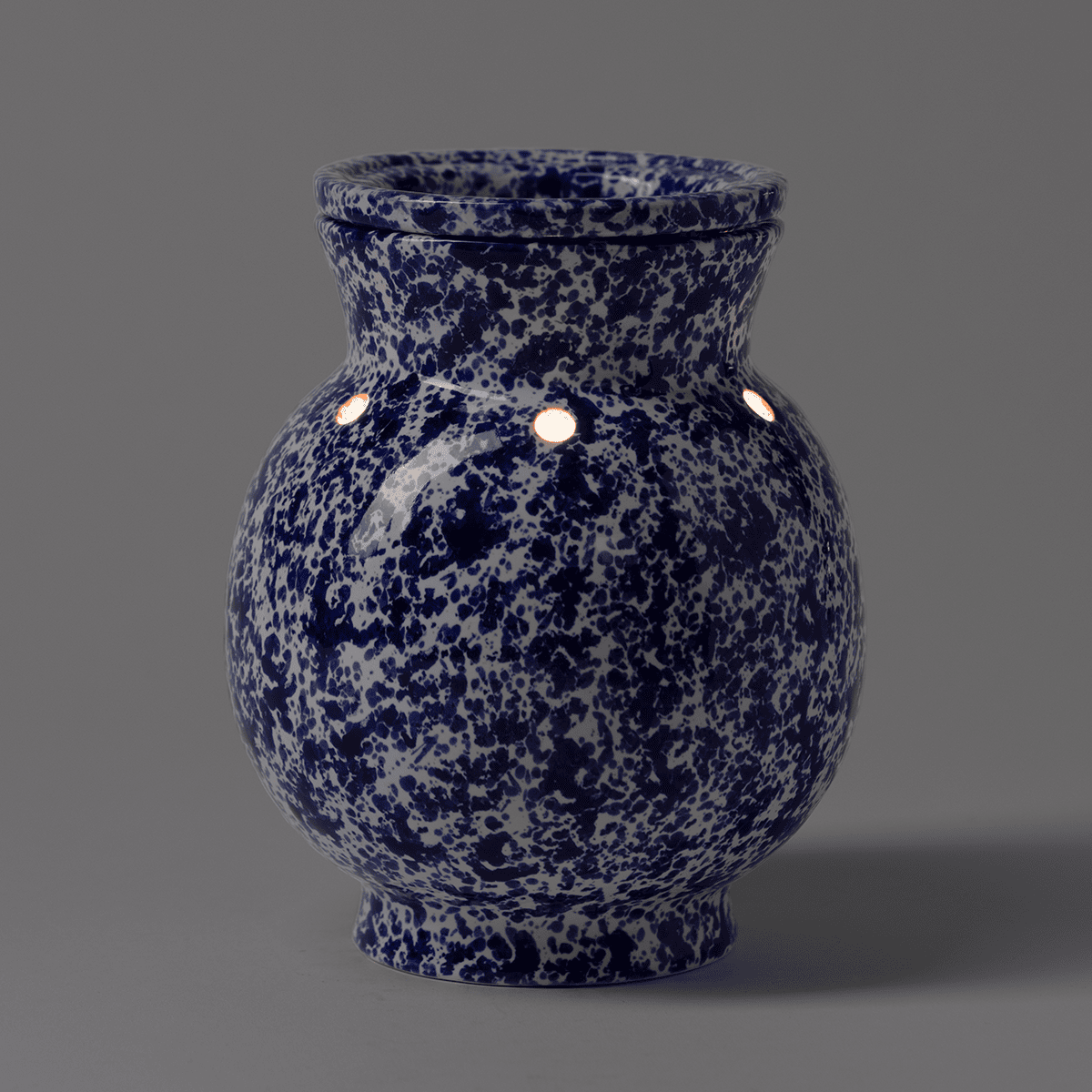 Blue Spongeware Scentsy warmer showing glow through decorative holes near the neck in a dark room