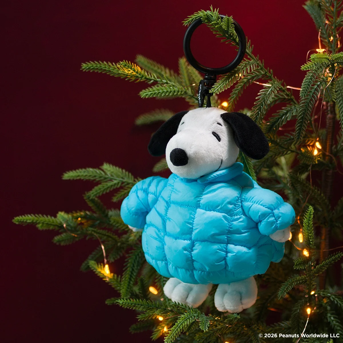 Snoopy Scentsy Buddy Clip wearing a bright blue puffer jacket, hanging on a Christmas tree