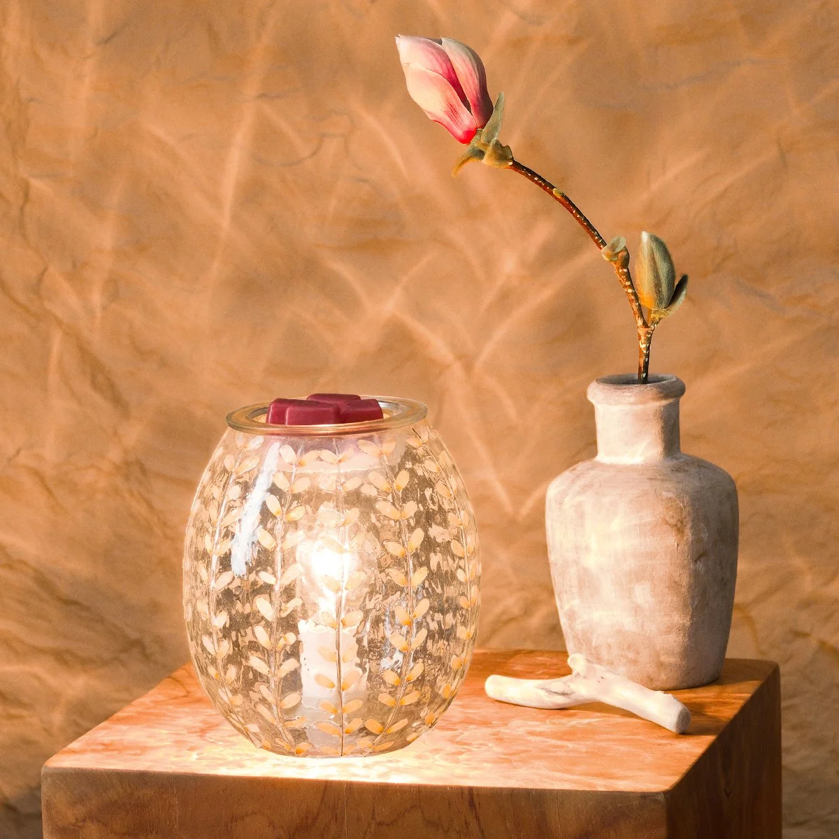 White Marigold Scentsy Warmer styled on a tabletop with decorative vase, glowing brightly and casting patterned light