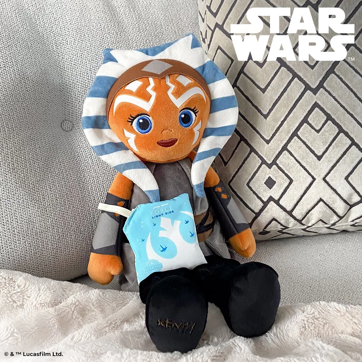 Ahsoka Scentsy Buddy sitting on a couch holding Light Side of the Force scent pak in a cozy home setting