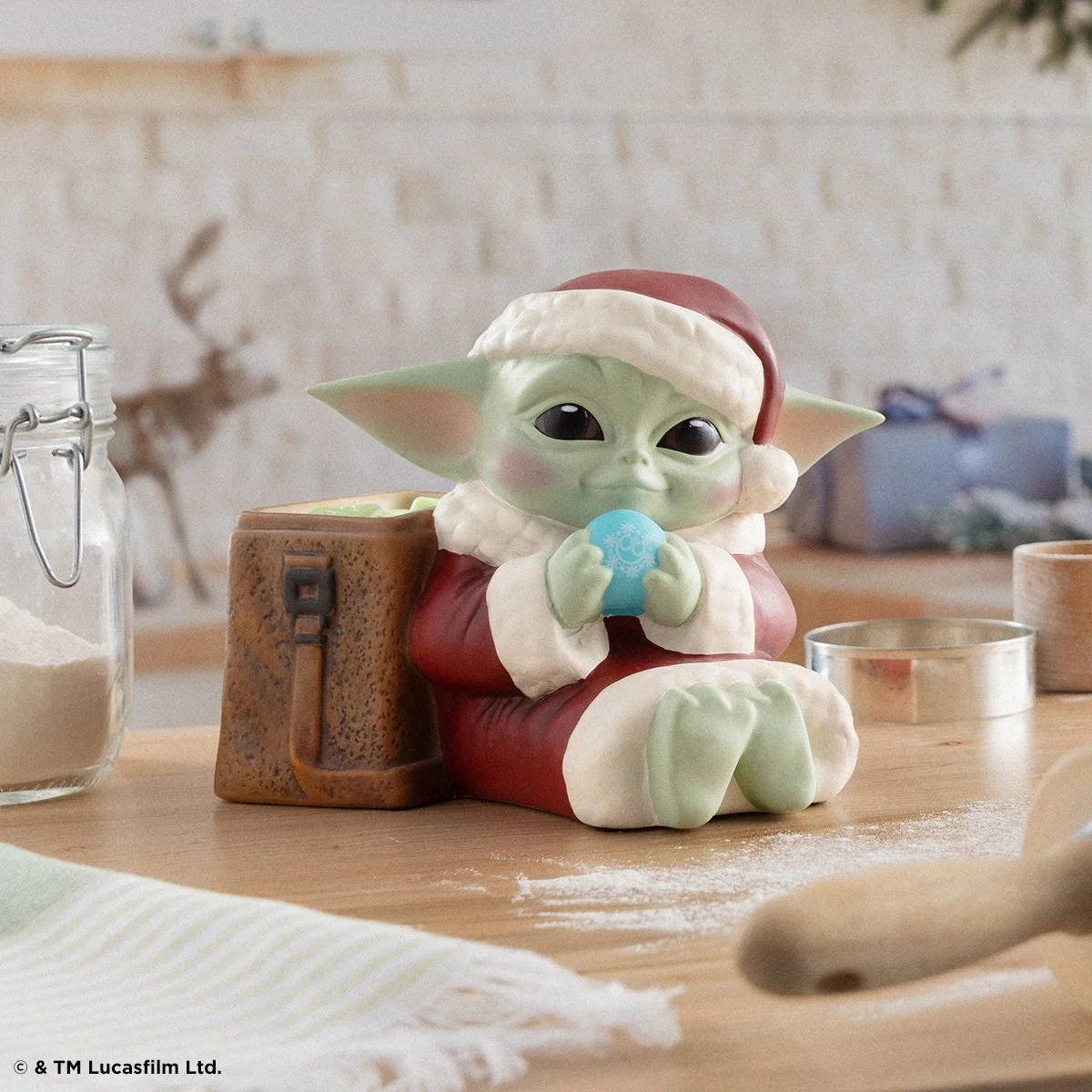 Grogu holiday Scentsy warmer holding a festive ornament in a soft kitchen setting with baking elements