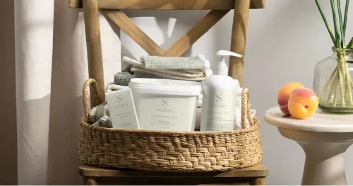 Scentsy laundry care products arranged in a woven basket with folded towels