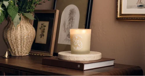 Glowing Scentsy scented candle with decorative floral design on a wooden side table