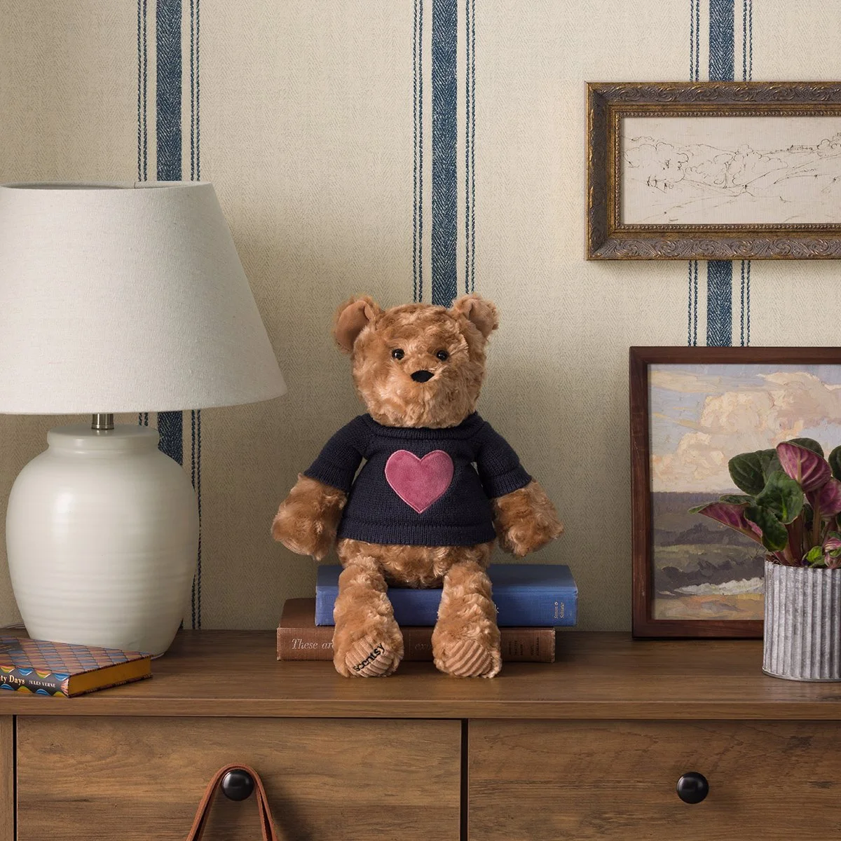 Banner the Bear Scentsy Buddy displayed on a wooden dresser in a cozy home setting, wearing a navy sweater with a pink heart design