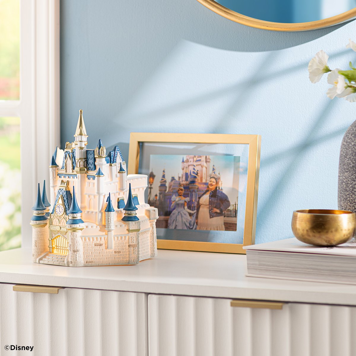 The Cinderella Castle Scentsy Warmer styled on a dresser with a framed photo of the Walt Disney World castle